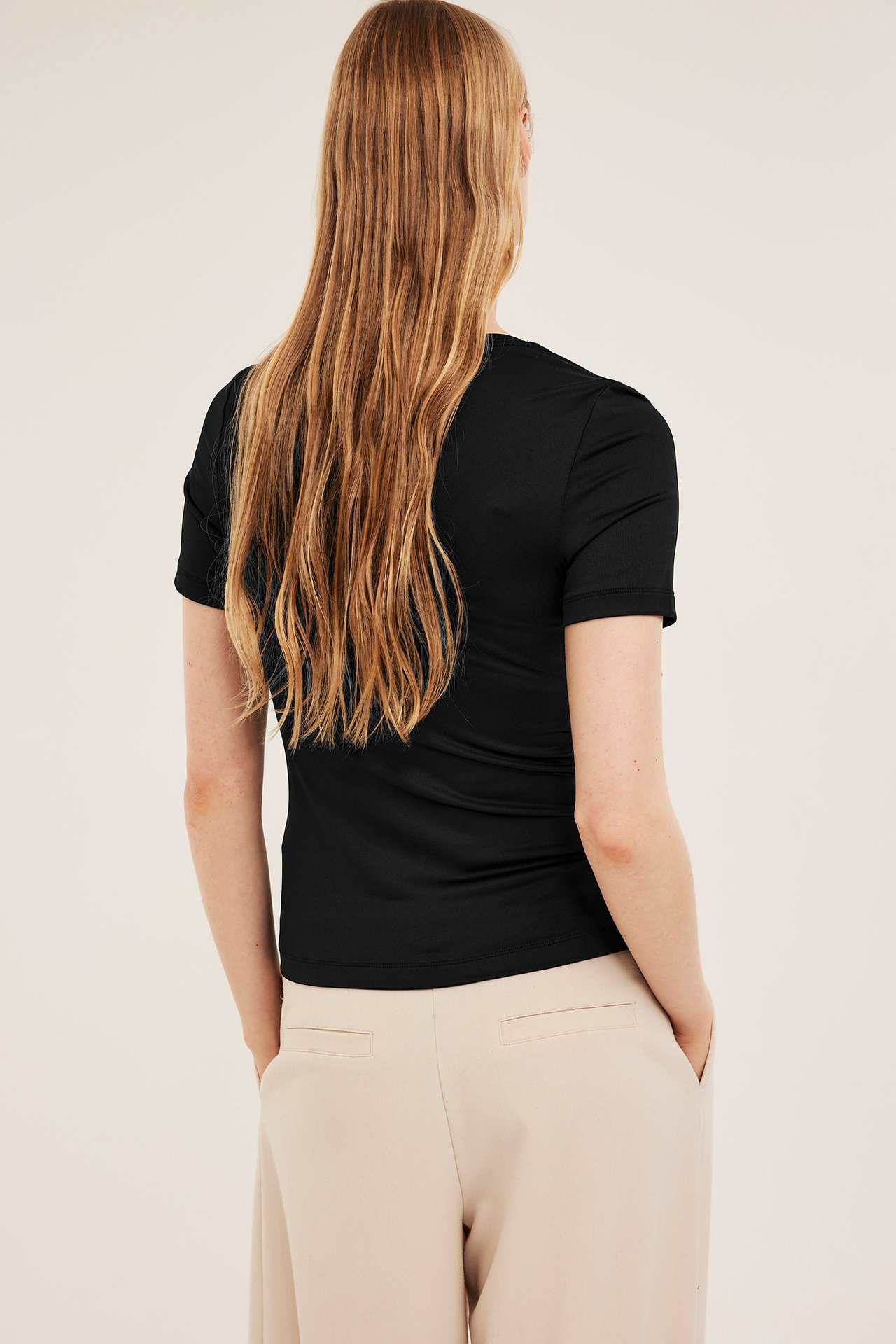 Nainen takaa, yllään musta ribattu lyhythihainen t-paita ja beiget leveälahkeiset housut.