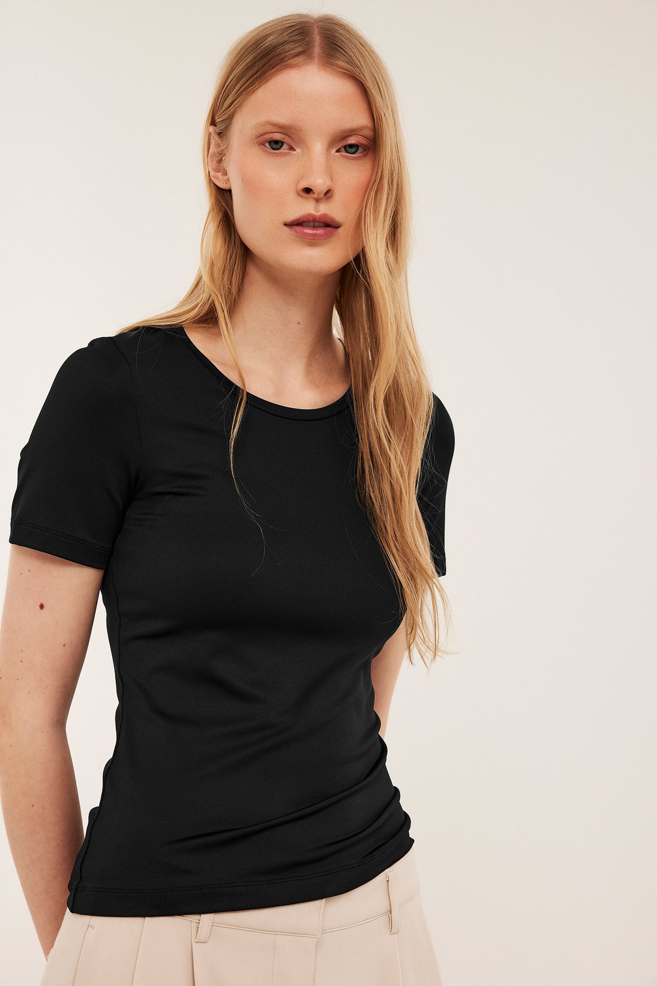 Edestä kuvattu nainen yllään istuva musta ribattu t-paita ja vaaleanbeiget housut.