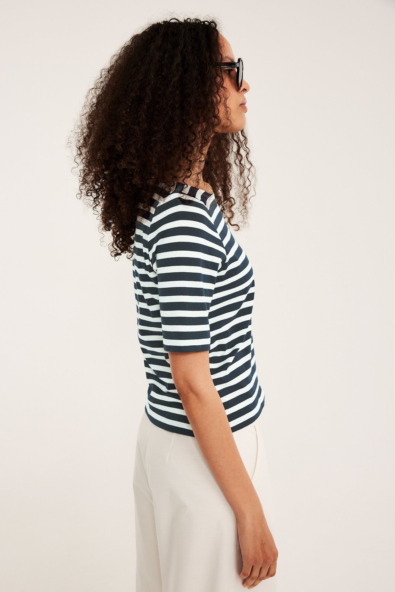 Sivukuva: Nainen tummansinisessä ja valkoisessa raidallisessa venekaulapuserossa, beigeissä housuissa, mustat aurinkolasit.