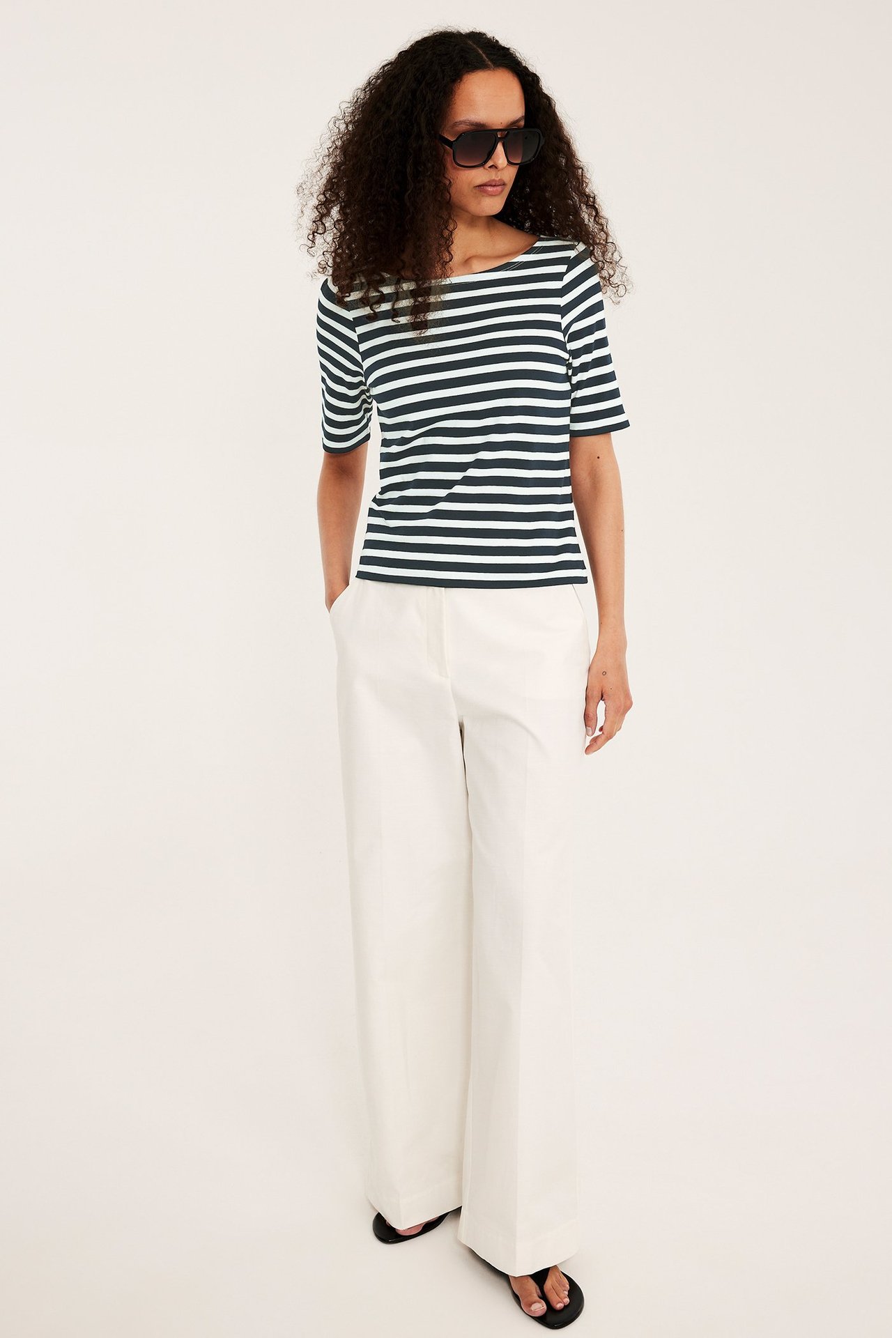 Edestä: Nainen yllään tummansininen ja luonnonvalkoinen raidallinen venepääntiepusero, luonnonvalkoiset leveät housut, mustat sandaalit.