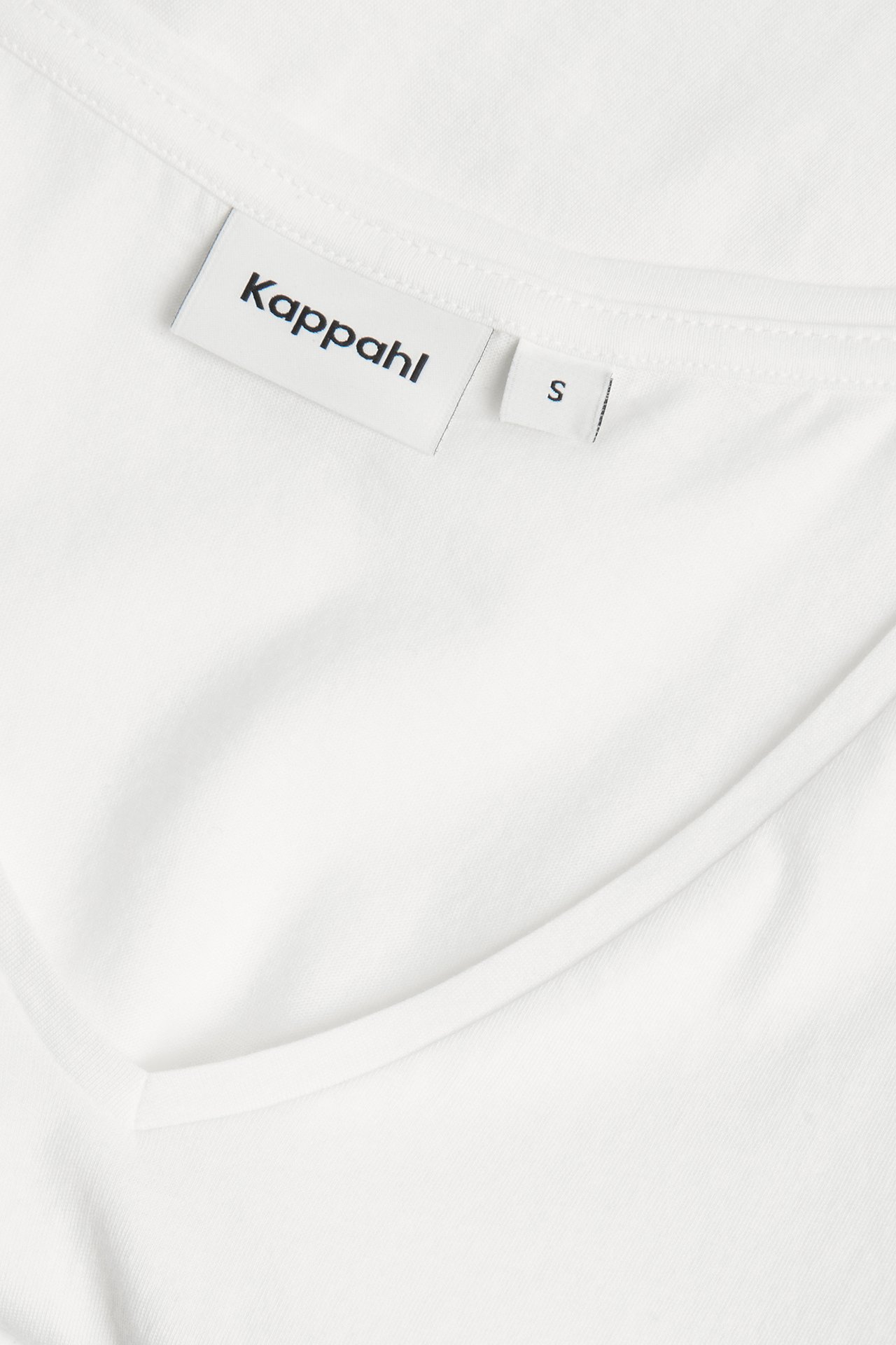 Närbild av en vit bomulls-V-ringad t-shirt med synlig märkeslapp vid halsringningen.