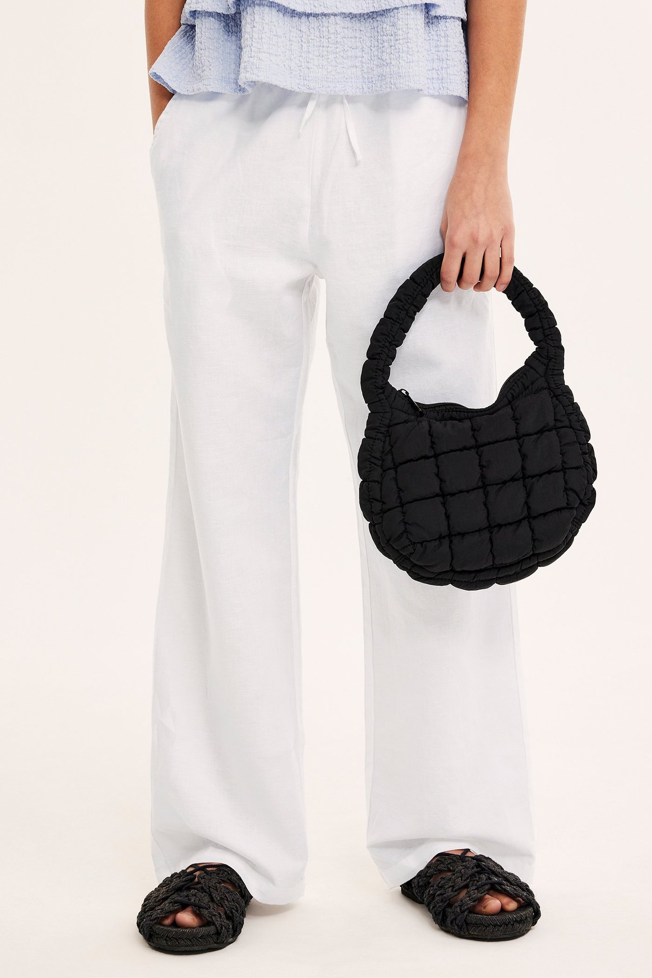 Edestä: Valkoiset pellavasekoitehousut, vaaleansininen toppi, musta tikattu laukku ja mustat punotut sandaalit.