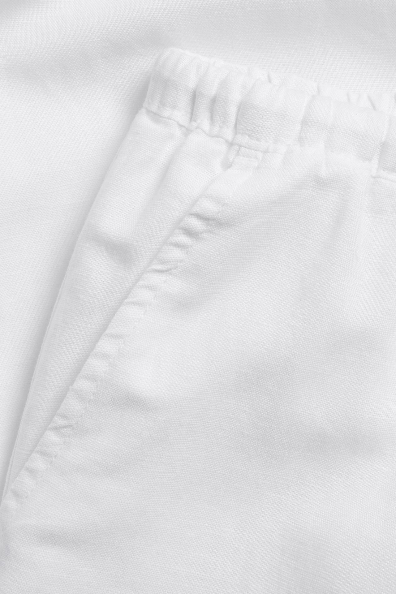 Zbliżenie białych spodni z mieszanki lnu z elastyczną talią i przednią kieszenią.