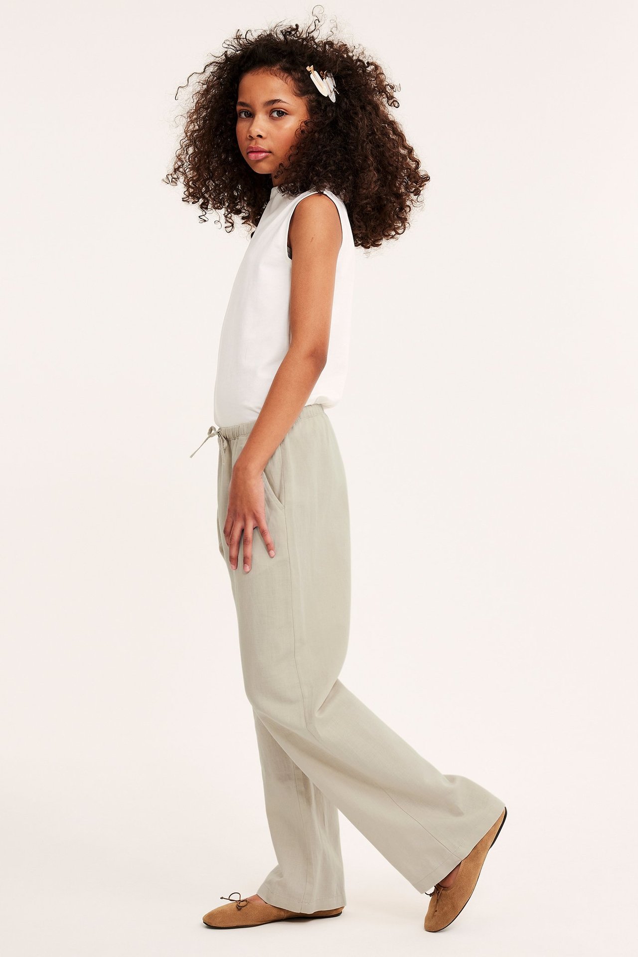 Sivukuva lapsesta beigenvärisissä pellavasekoitehousuissa, joissa kiristysnyöri, valkoinen hihaton toppi ja ruskeat kengät.