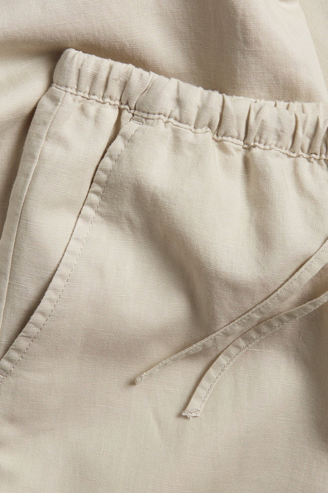 Zbliżenie beżowych spodni z mieszanki lnu z elastyczną talią ze sznurkiem i przednimi kieszeniami.
