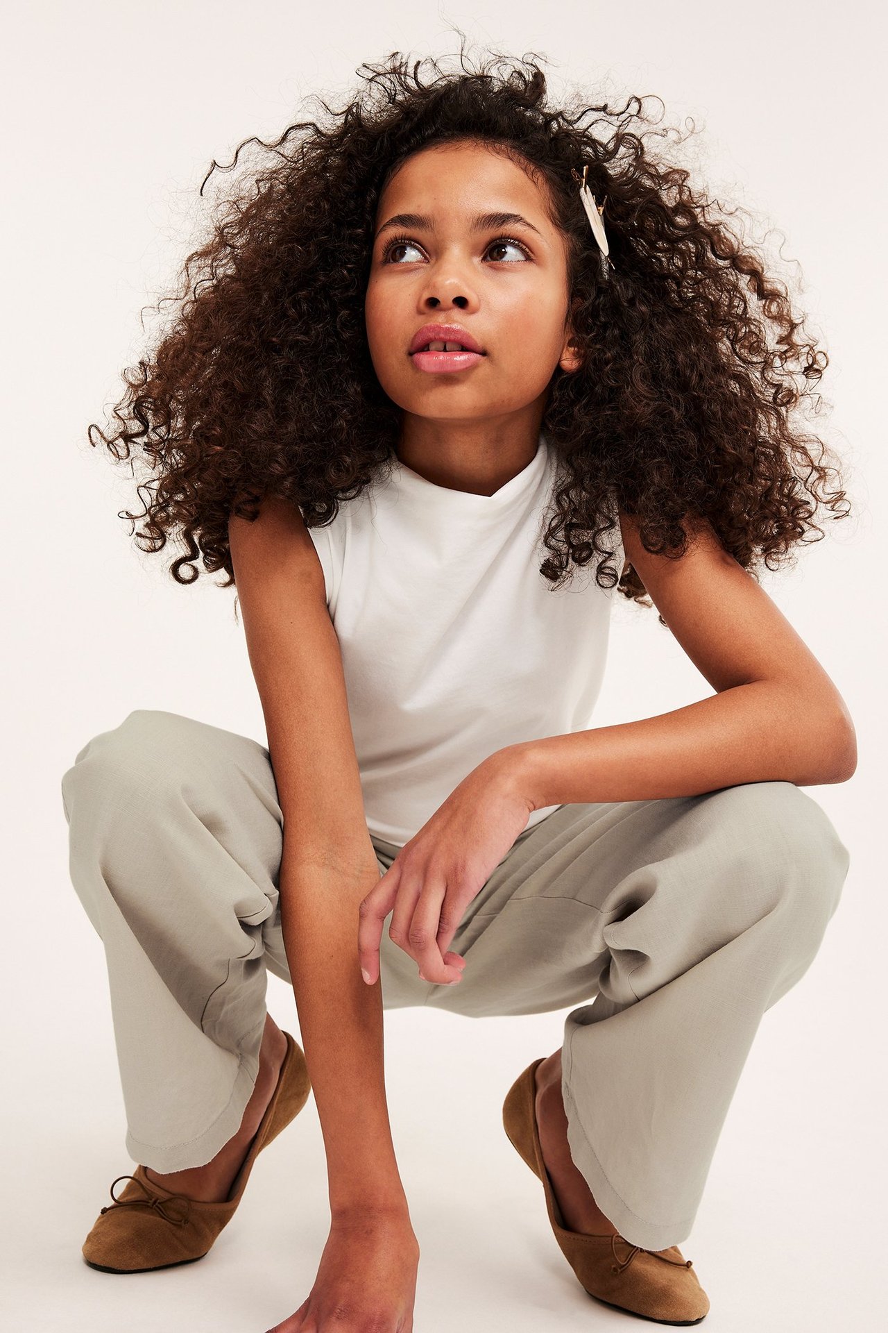 Edestäpäin: lapsi yllään rennot beiget pellavasekoitehousut, valkoinen hihaton toppi ja ruskeat ballerinat.