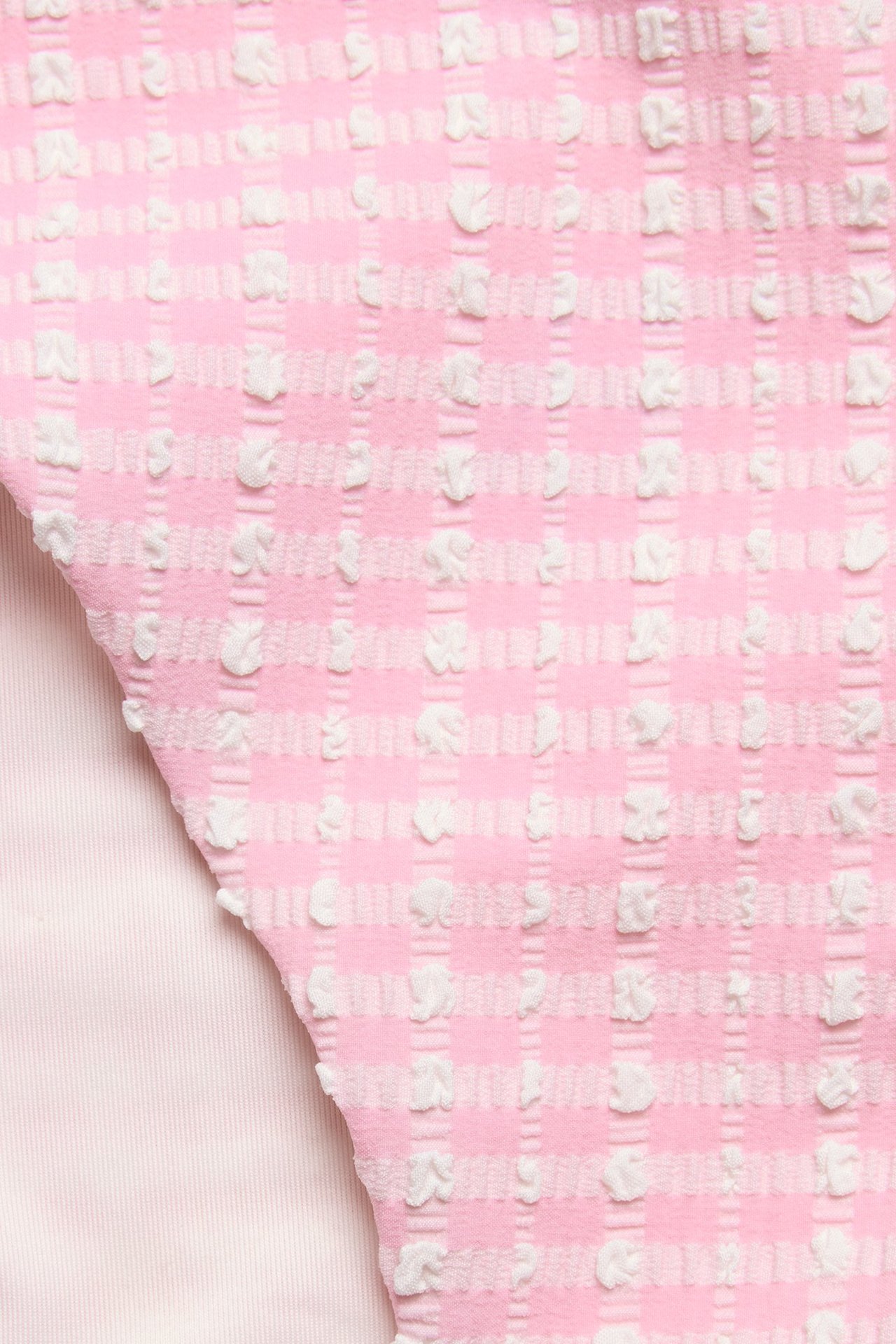 Zbliżenie na jasnoróżowy materiał majtek bikini z białym, teksturowanym wzorem w kratę.