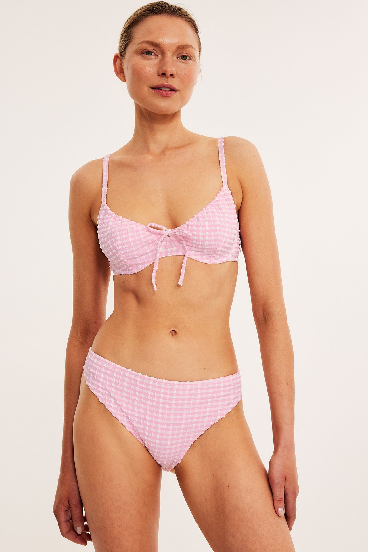 Widok z przodu kobiety w jasnoróżowych, w kratkę, brazylijskich figach bikini i pasującym biustonoszu.