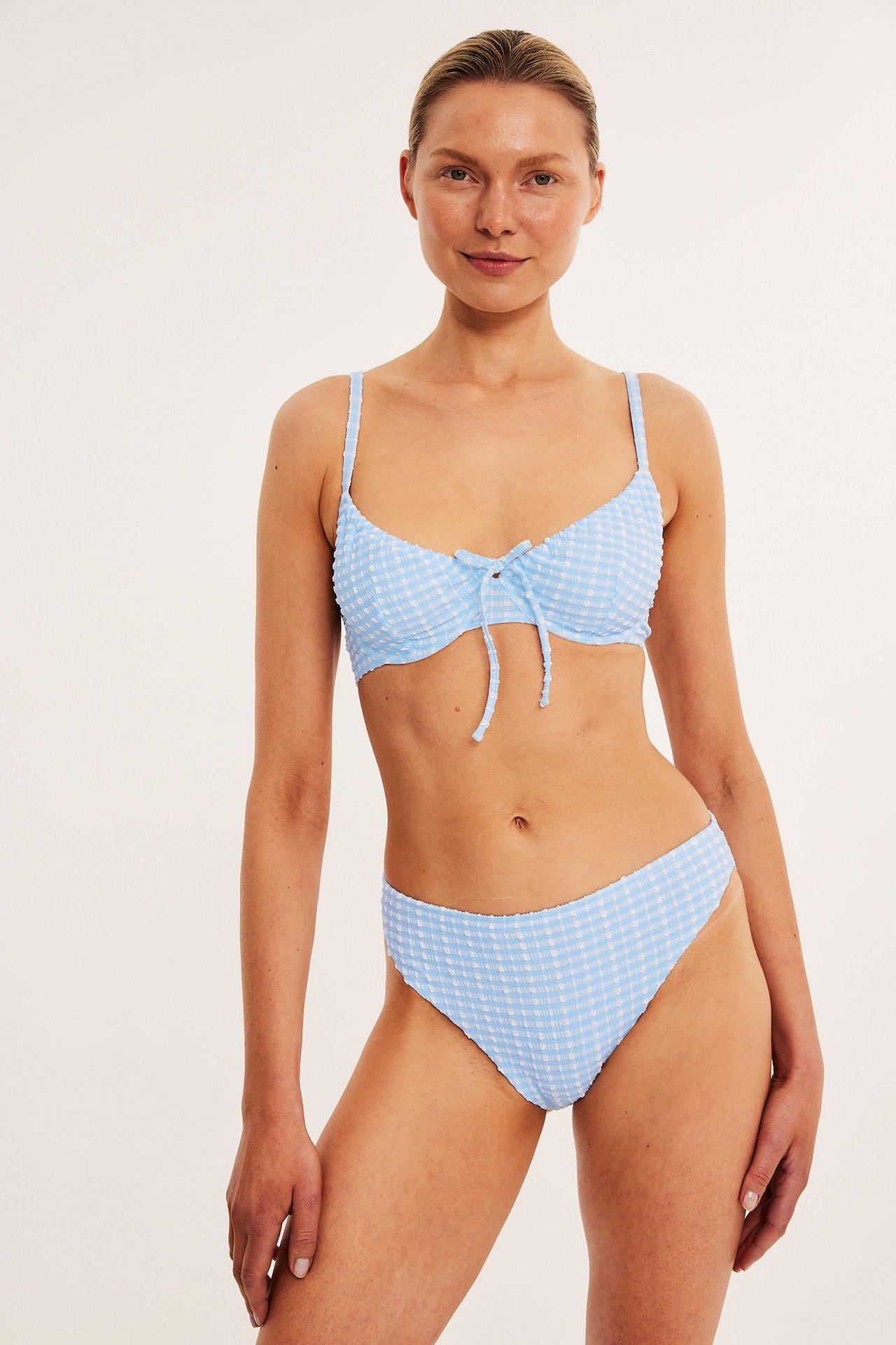 Widok z przodu kobiety w jasnoniebieskich, kraciastych figach bikini Brazilian i pasującej górze.