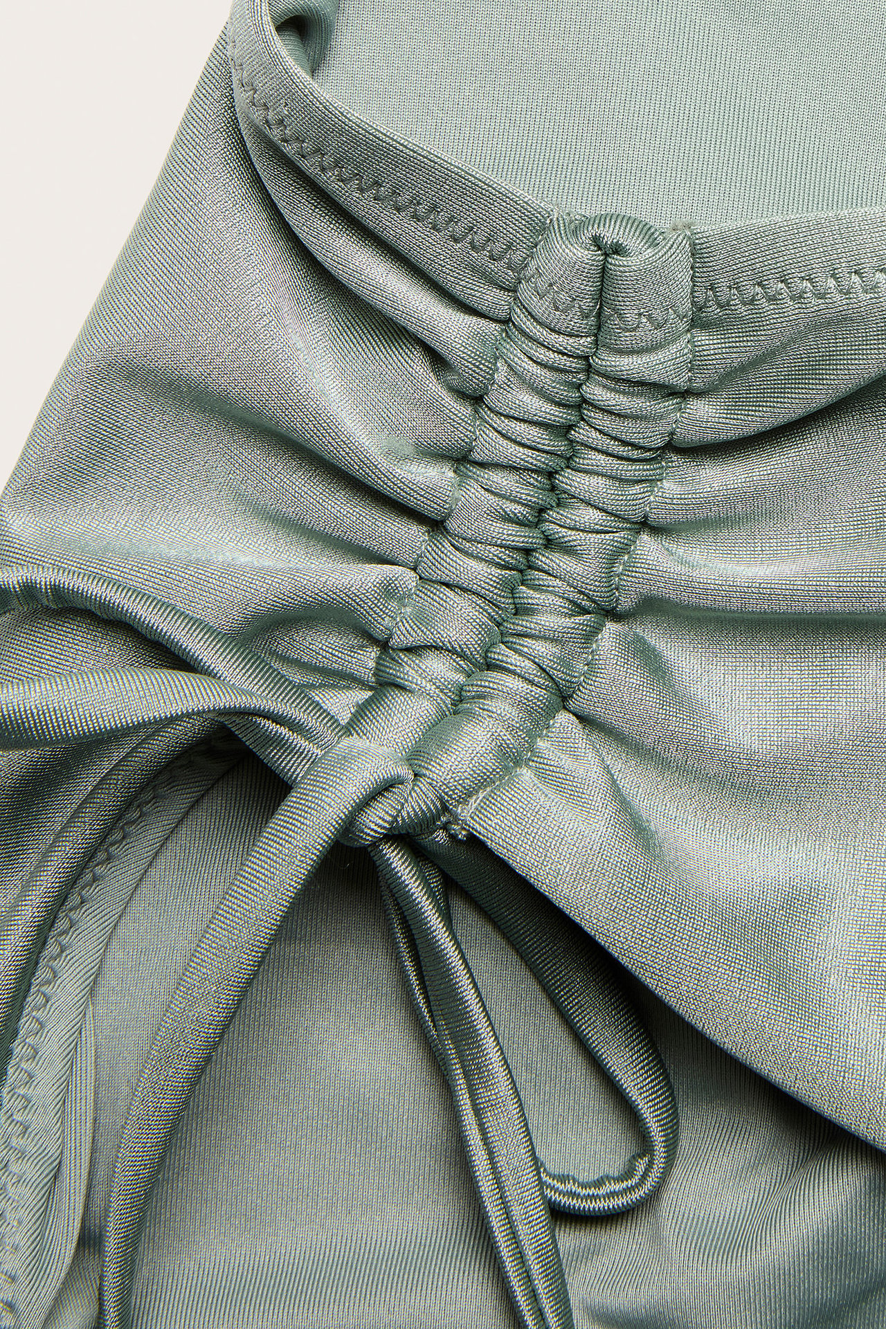 Zbliżenie na jasnozielone, błyszczące figi bikini z marszczonym bokiem i wiązaniem.