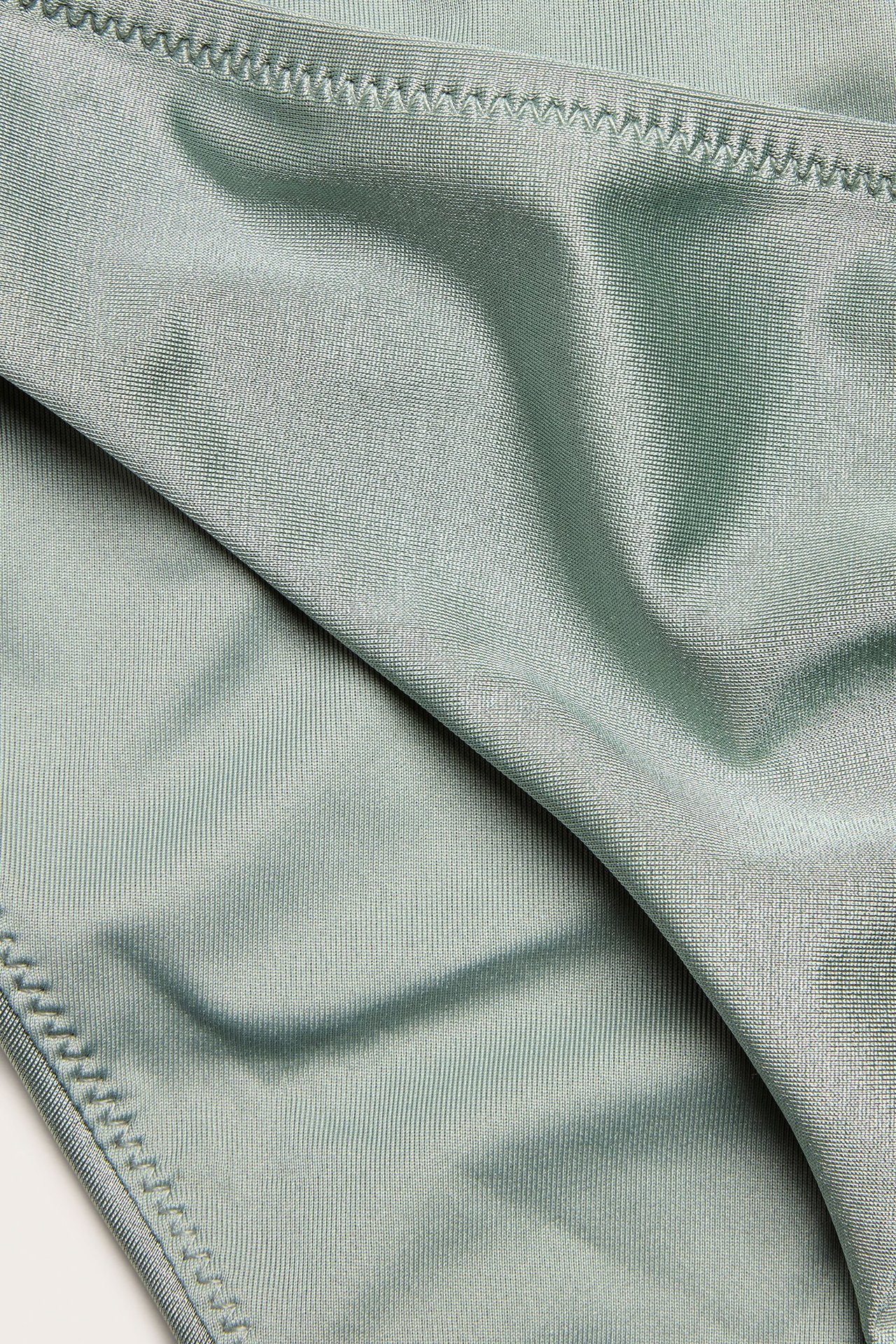 Zbliżenie na jasnozielony, jednolity materiał od majtek bikini z widocznymi szwami.