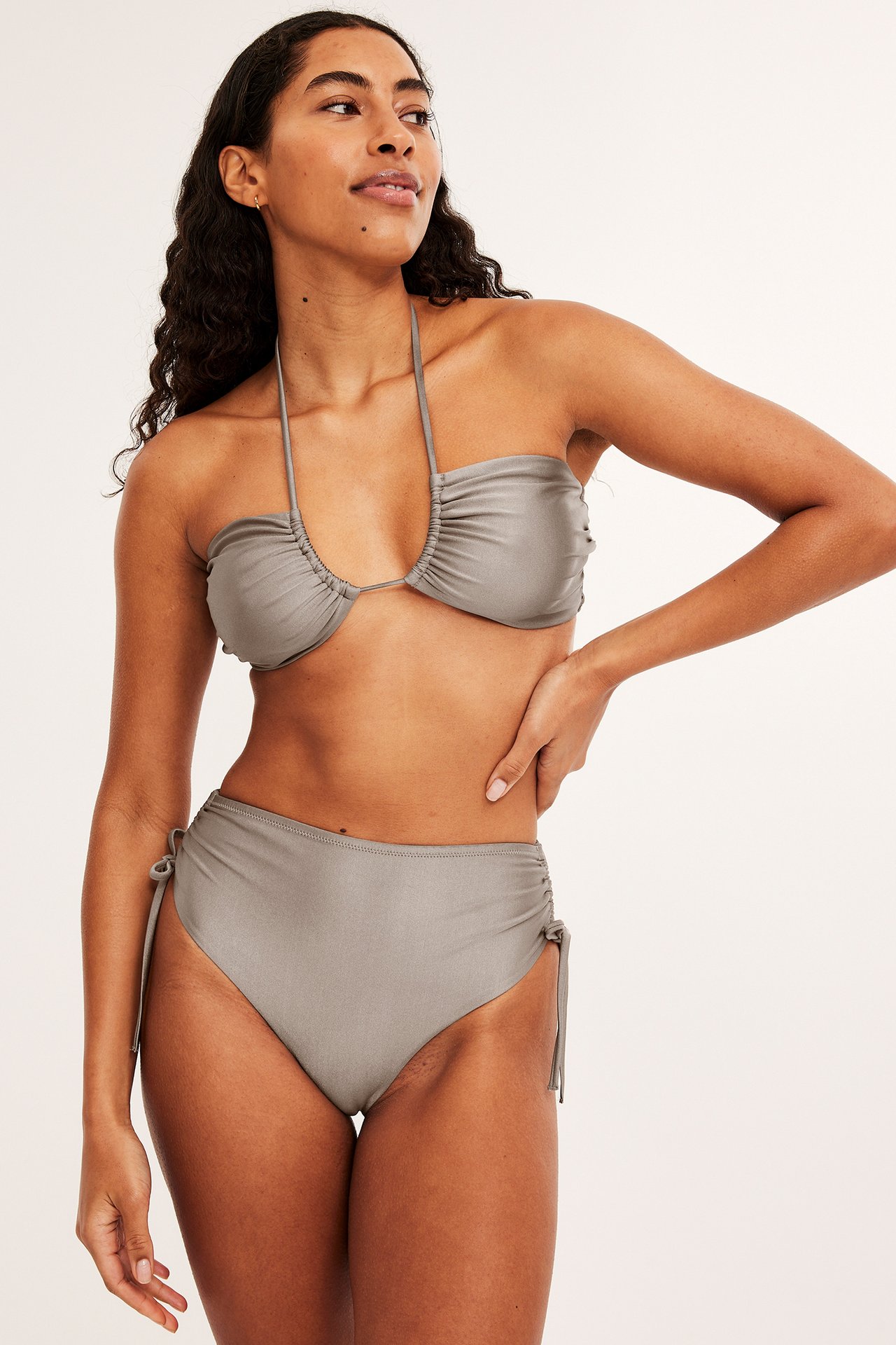 Framifrån, kvinna i glansig mörkbeige bandeau bikinitopp med nackband och matchande hög midja trosa.