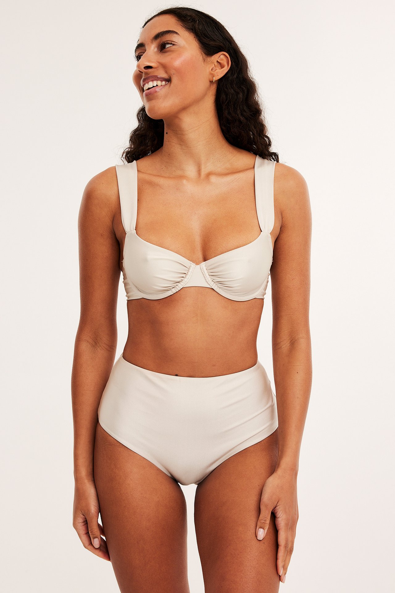 Kvinne iført en beige bøyle-bikinitopp med brede stropper og matchende høytlivs bikinitruse.