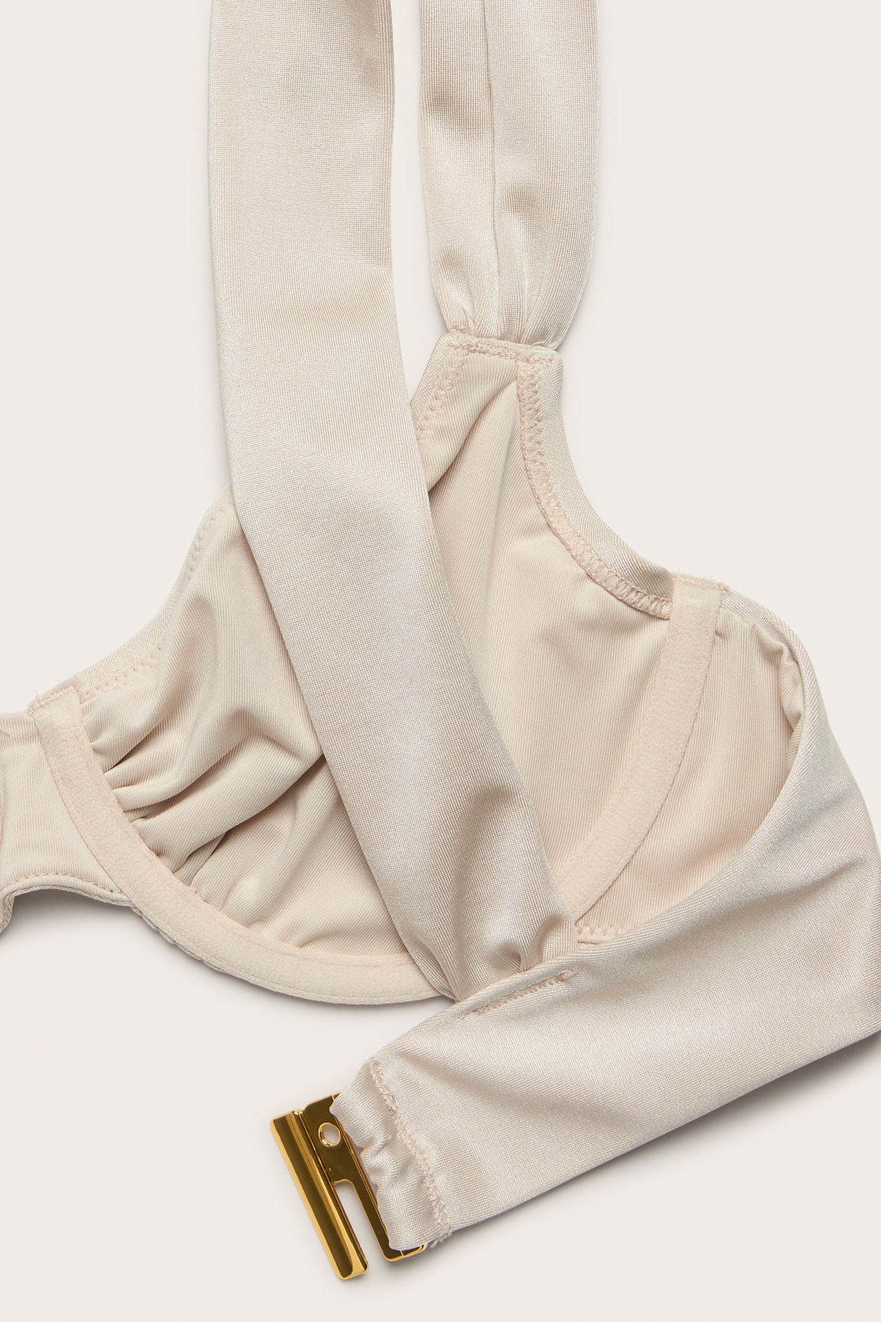 Nærbilde av en beige bøyle-bikini-BH med draperte cuper og gullfarget ryggspenne.