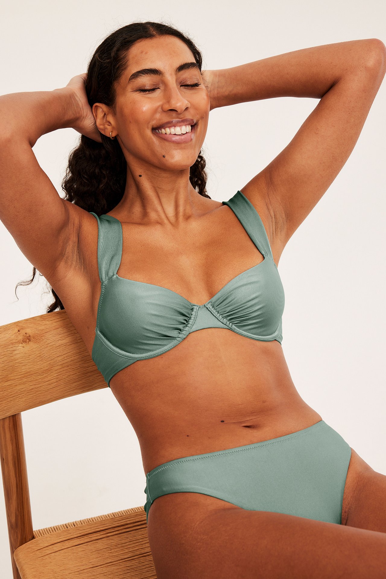 Framifrån, leende kvinna i ljusgrön draperad bygel-bikiniöverdel och matchande underdel.