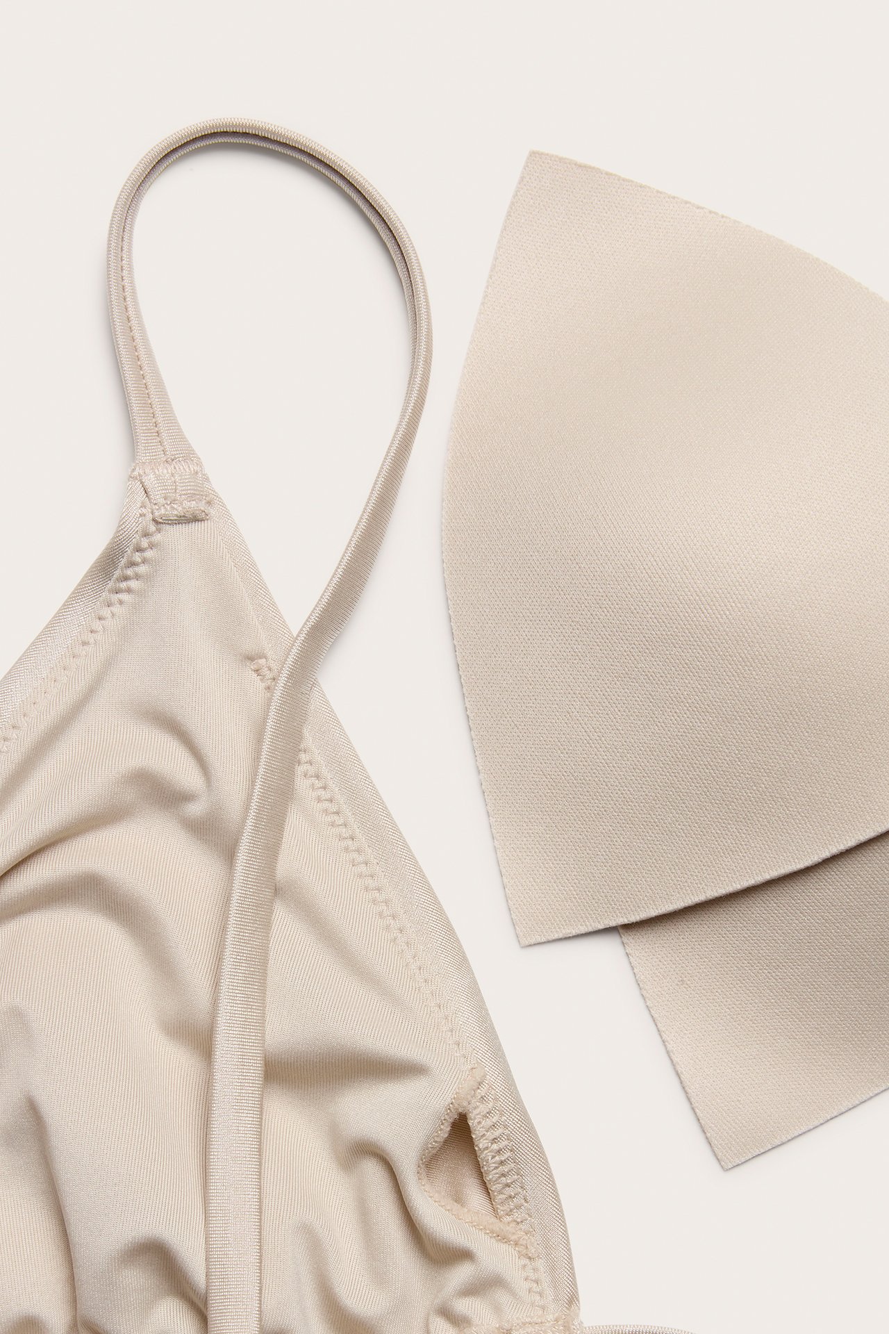 Zbliżenie beżowego, błyszczącego biustonosza bikini typu trójkąt z cienkimi ramiączkami i wyjmowaną beżową wkładką.