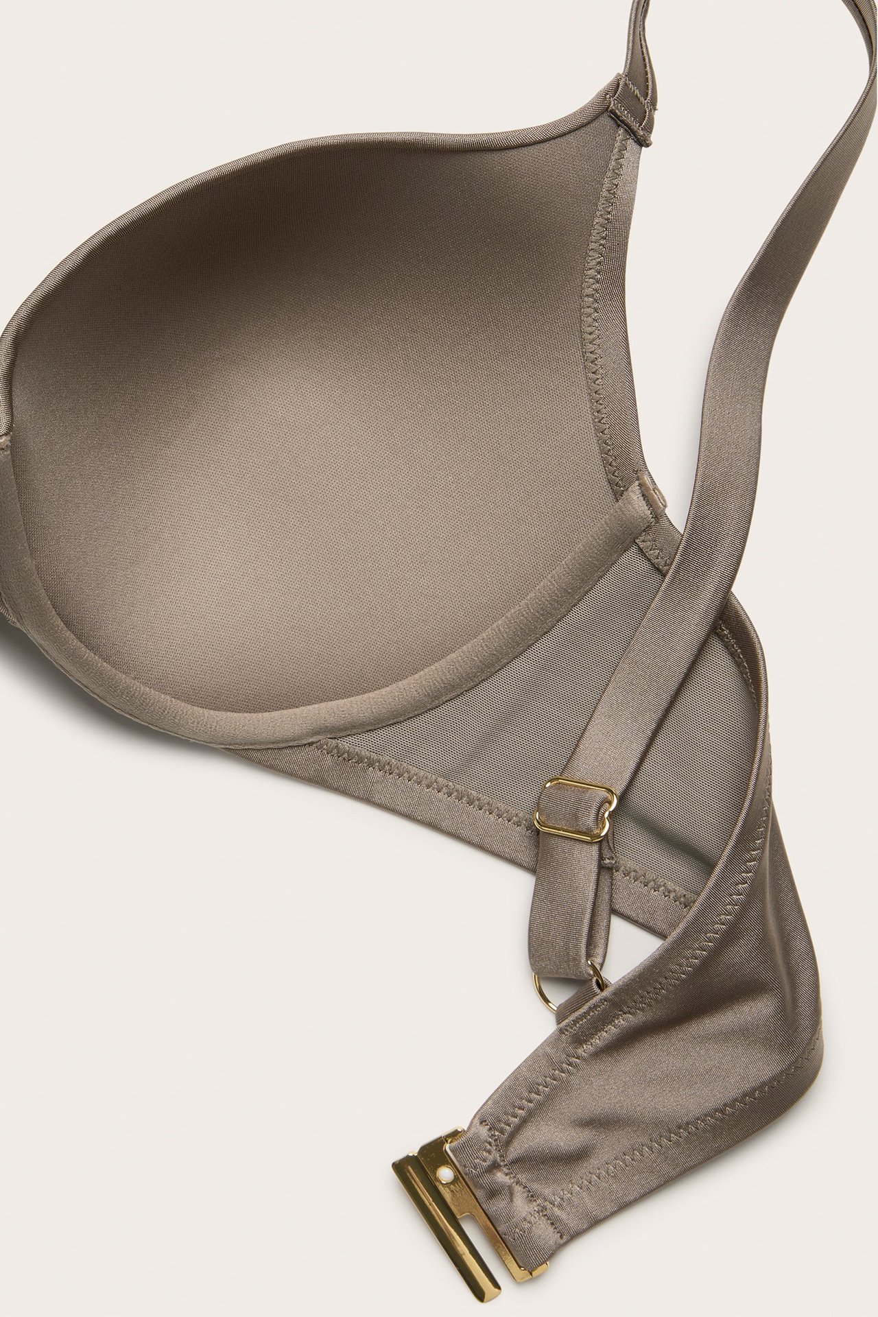 Zbliżenie na ciemnobeżowy wyściełany biustonosz bikini z regulowanym ramiączkiem i złotym zapięciem.