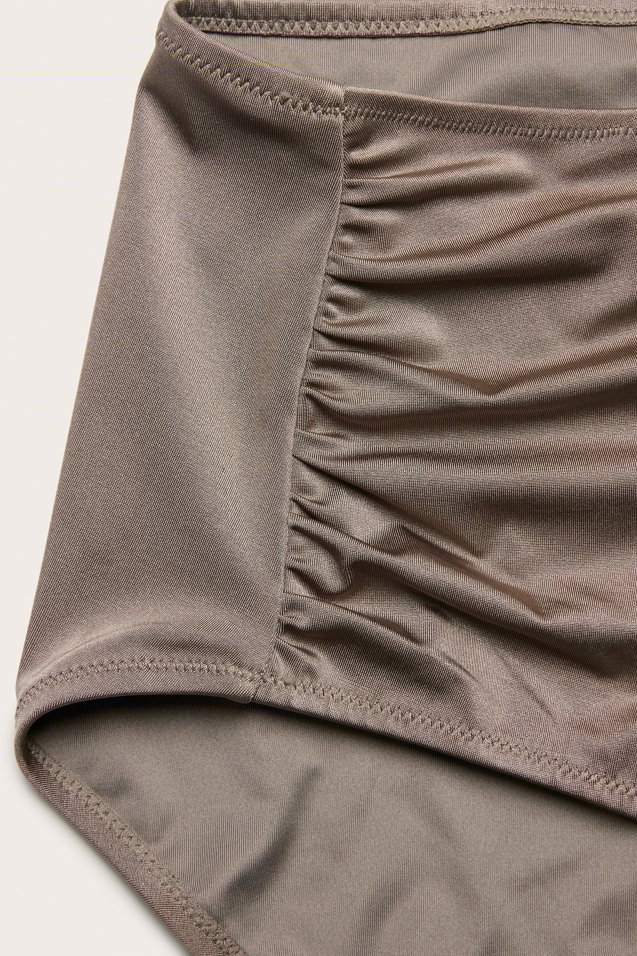 Zbliżenie na ciemnobeżowe figi kąpielowe z wysokim stanem i marszczeniem po boku.