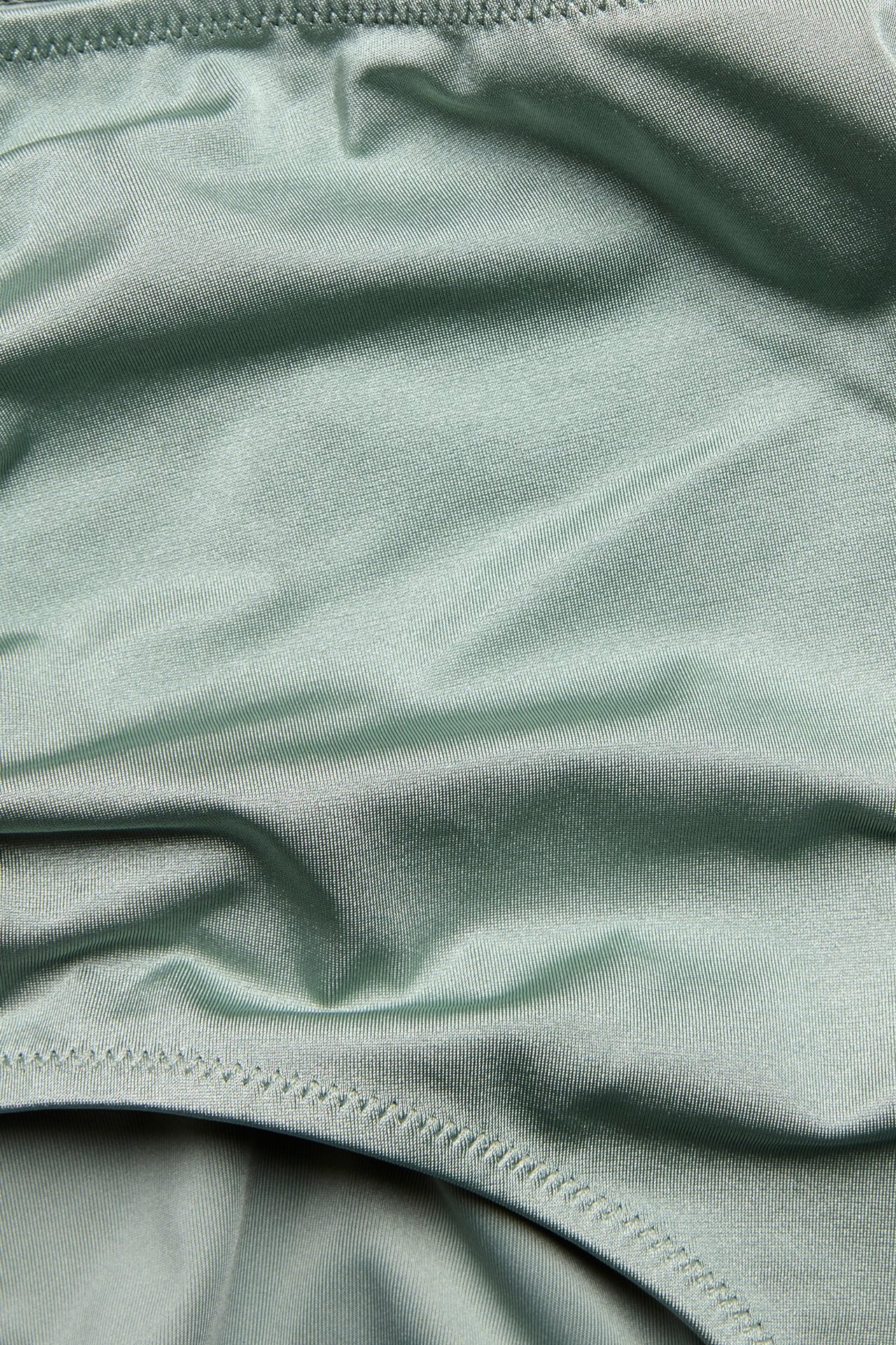 Zbliżenie na jasnozielone, jednolite majtki kąpielowe z wysokim stanem, marszczeniem z boku i widocznymi szwami.