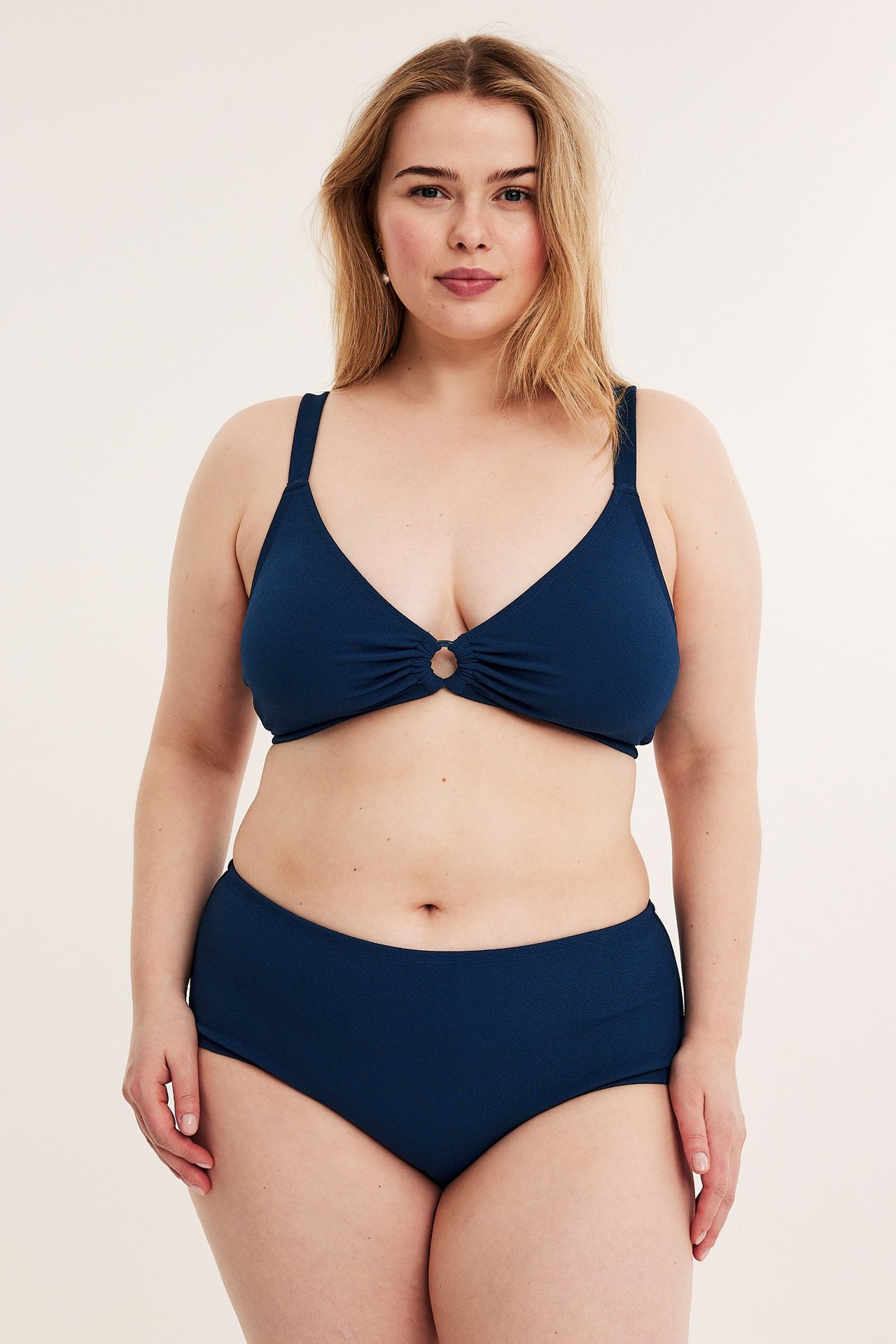 Widok z przodu: kobieta w granatowych, marszczonych, wysokich figach kąpielowych hipster i pasującym biustonoszu.