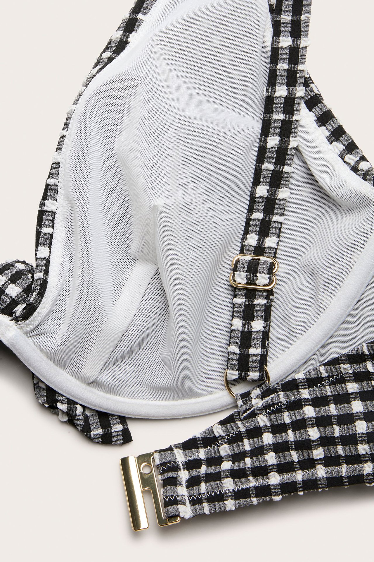 Zbliżenie czarno-białego, kraciastego, nieusztywnianego topu bikini ze złotymi regulowanymi ramiączkami i zapięciem.