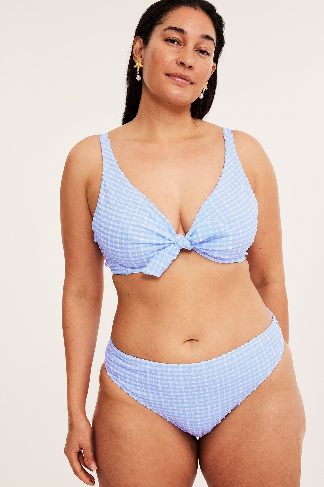 Widok z przodu: kobieta w jasnoniebieskim, kraciastym topie bikini z seersuckeru, pasującym dole i kolczykach.
