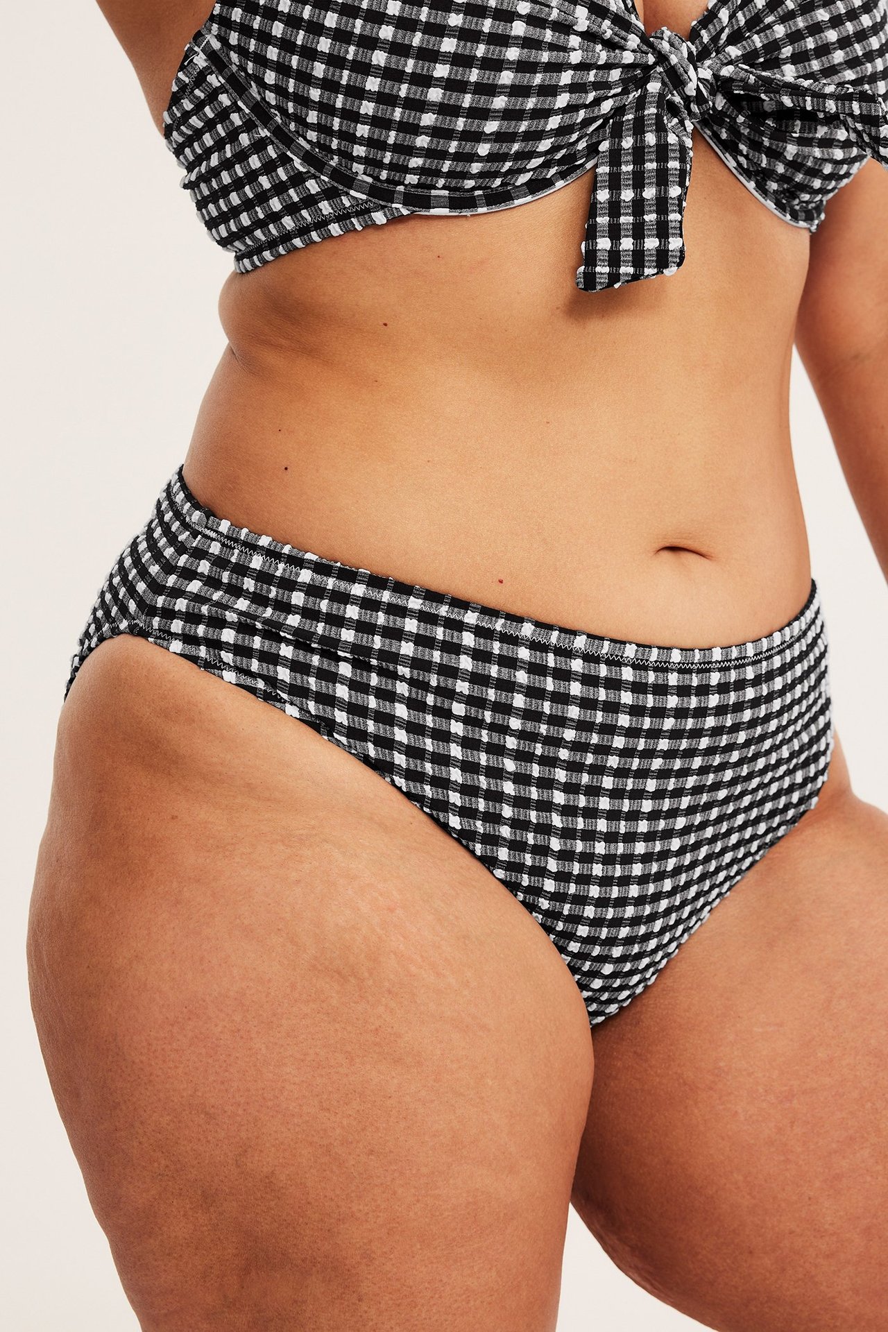 Frontbilde av kvinne i svart- og hvitrutet seersucker bikinitruse med høyt benkutt og matchende knyttet bikinitopp.