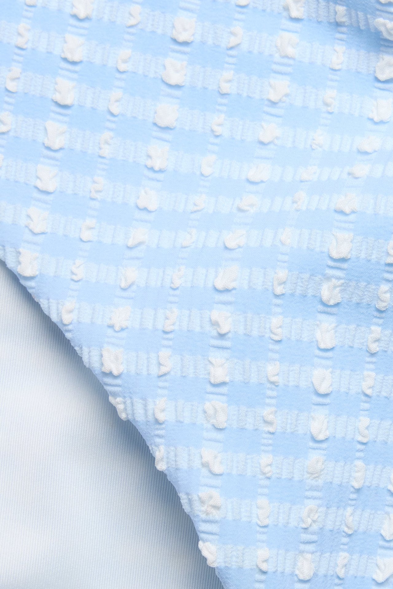 Zbliżenie na jasnoniebieskie i białe figi kąpielowe w kratę o fakturze seersucker.