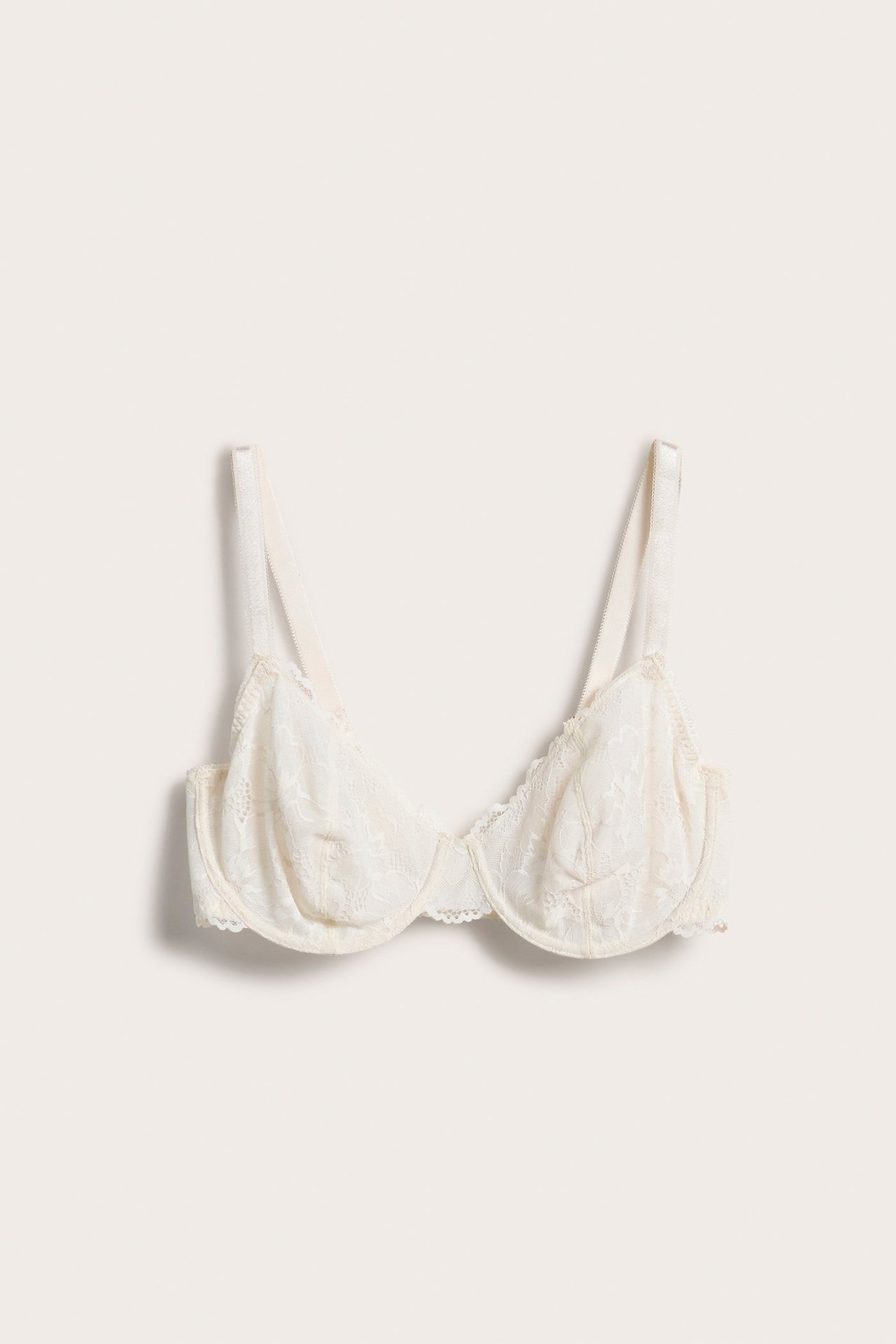 Widok z przodu białego, nieusztywnianego koronkowego biustonosza z fiszbinami i regulowanymi szerokimi ramiączkami.