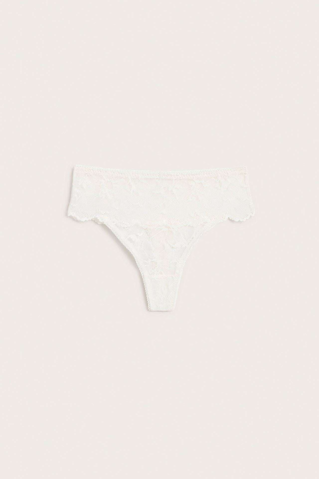 Frontbilde av en hvit blondestringtrusa med bred linning og bølgete kanter, flatlagt.