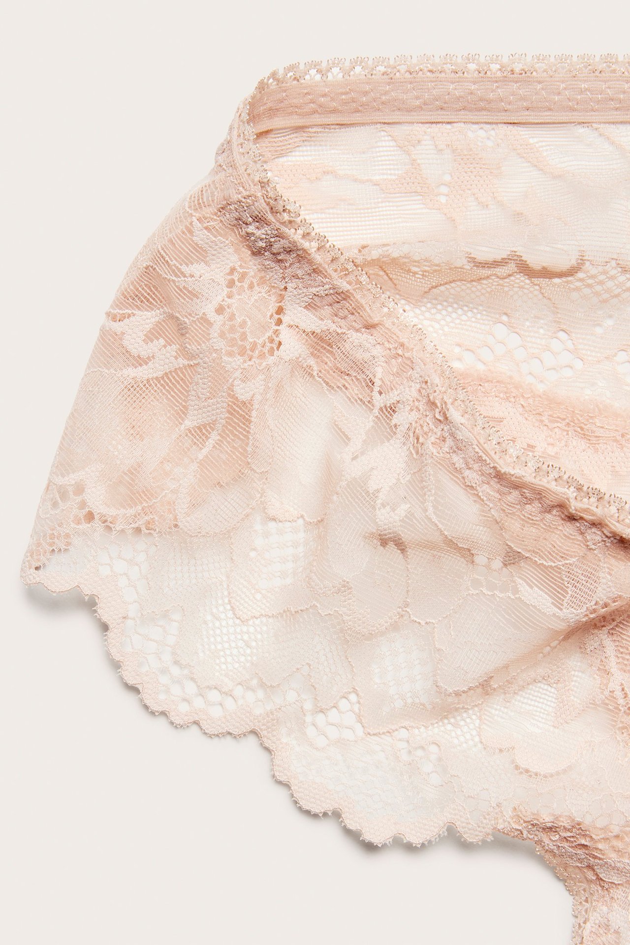 Zbliżenie różowych koronkowych stringów, ukazujące ich misterny wzór i falisty brzeg.