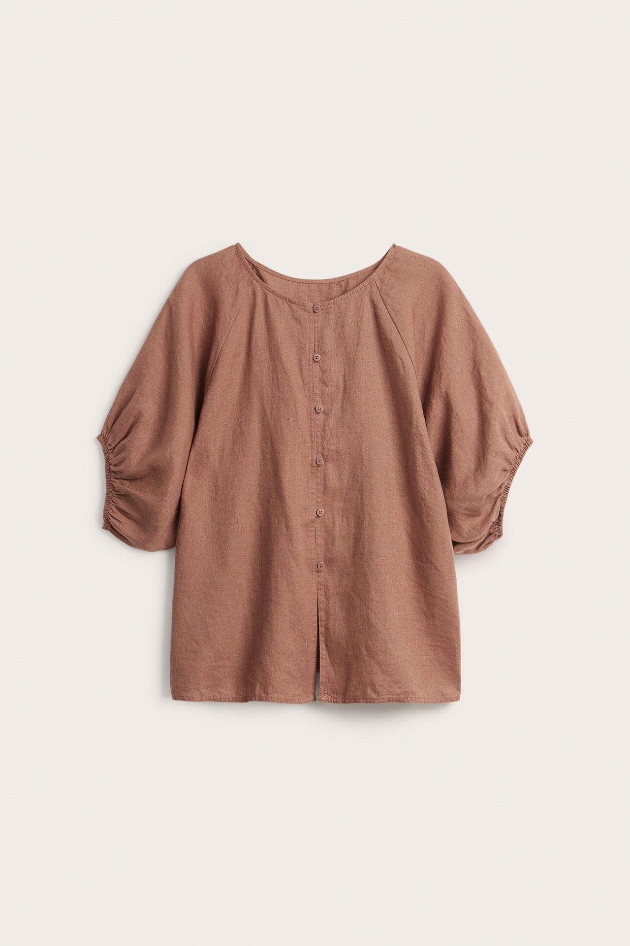 Frontvisning av en brun linbluse med rund hals, knapper foran og samlede halvlange ermer.