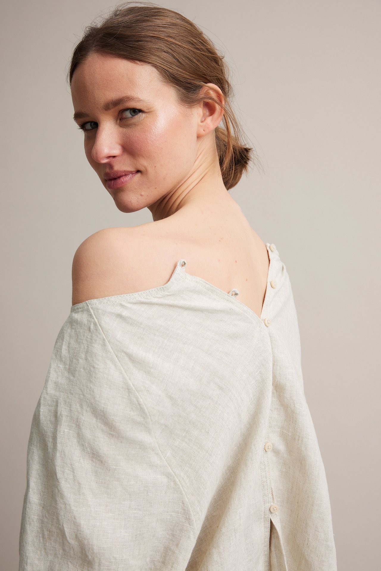 Bakifrån: kvinna i beige linneblus med knäppning, stylad off-shoulder.