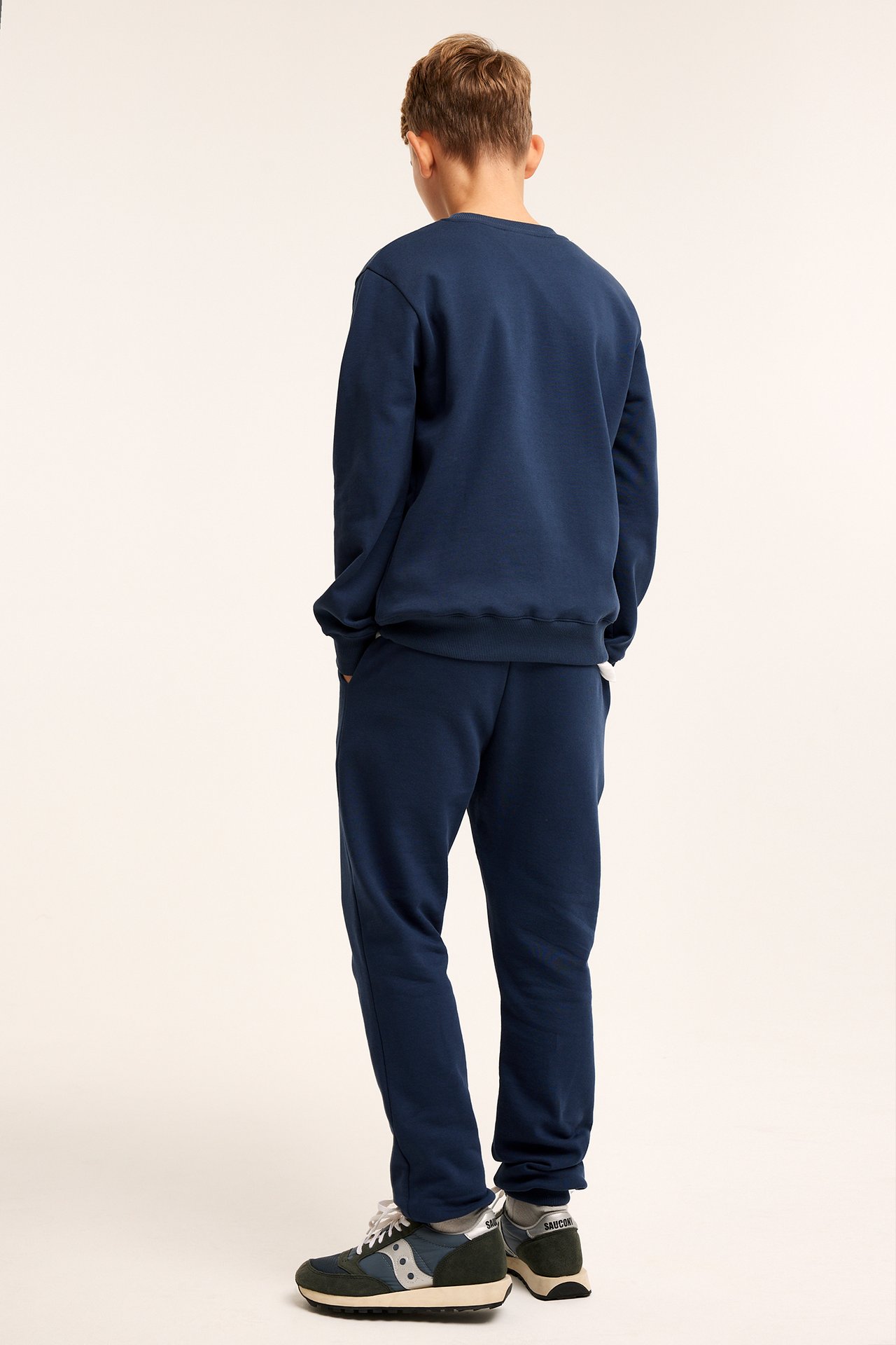 Bakifrån: ett barn i mörkblå mjukisbyxor med matchande mörkblå sweatshirt och sneakers.
