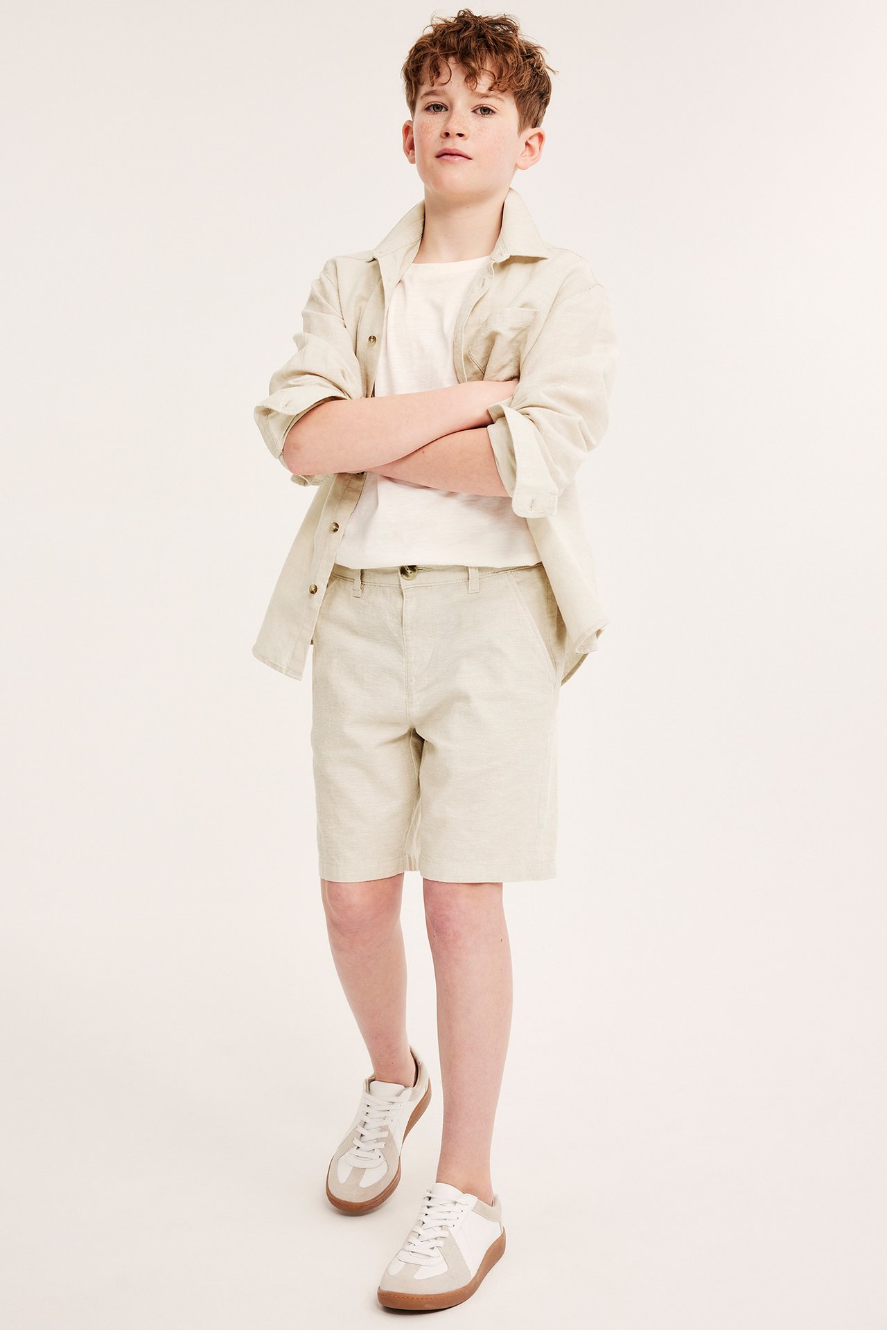 Frontvisning: Barn i lys beige linblanding shorts, hvit t-skjorte, åpen beige skjorte og hvite joggesko.