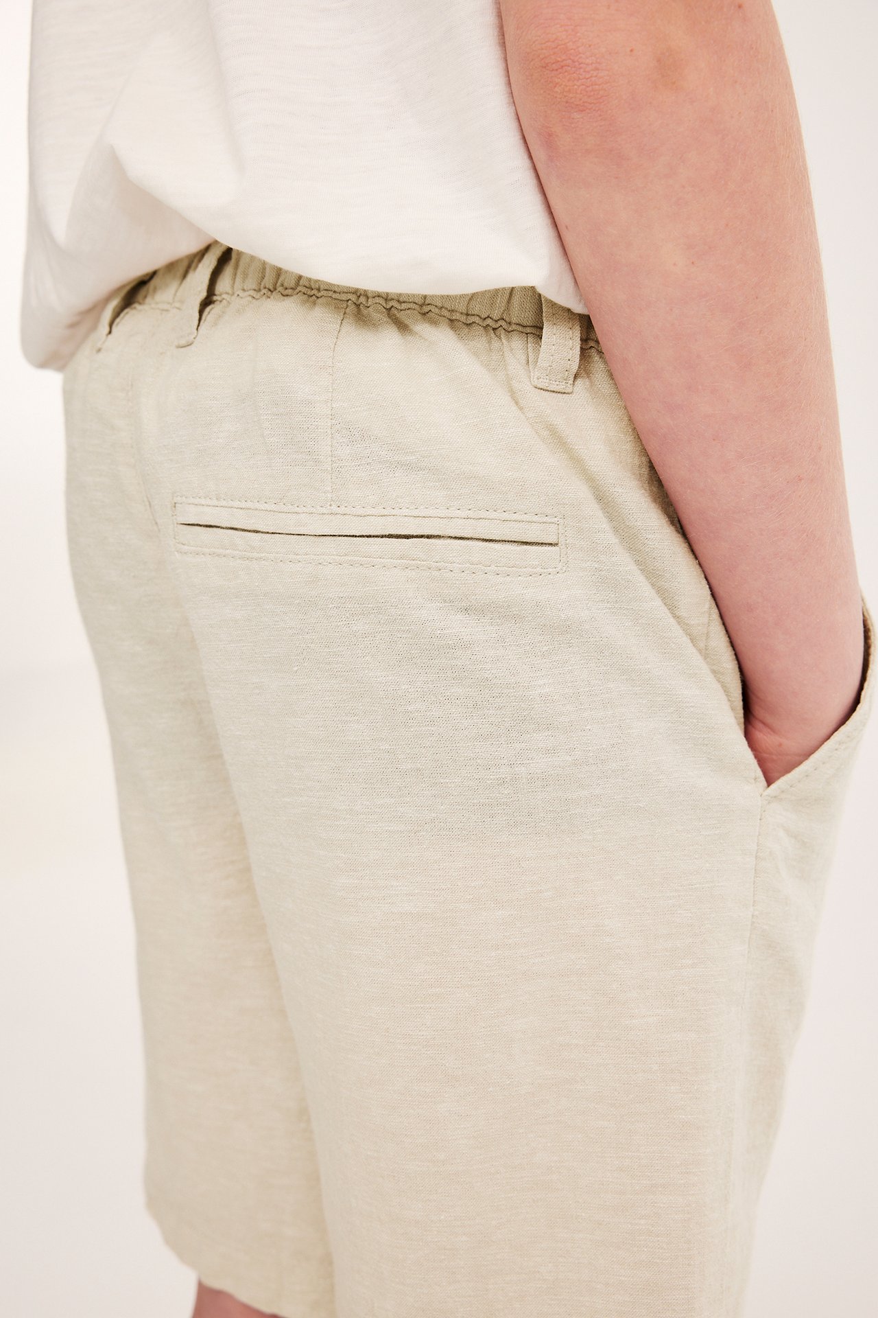 Sidevisning av barn i lysebeige linblandingsshorts med elastisk midje og fuskolomme bak.