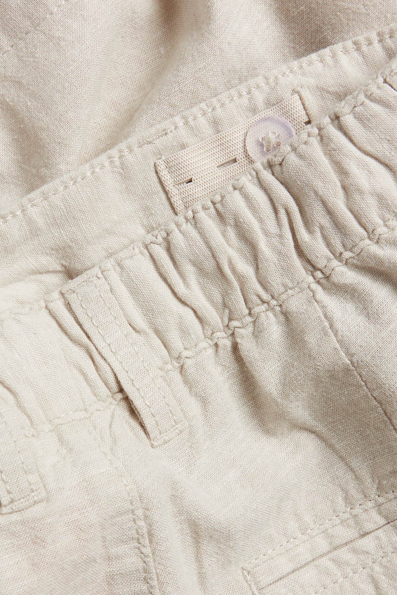 Nærbilde av lysebeige linblanding shorts med elastisk linning og justerbar knapp.