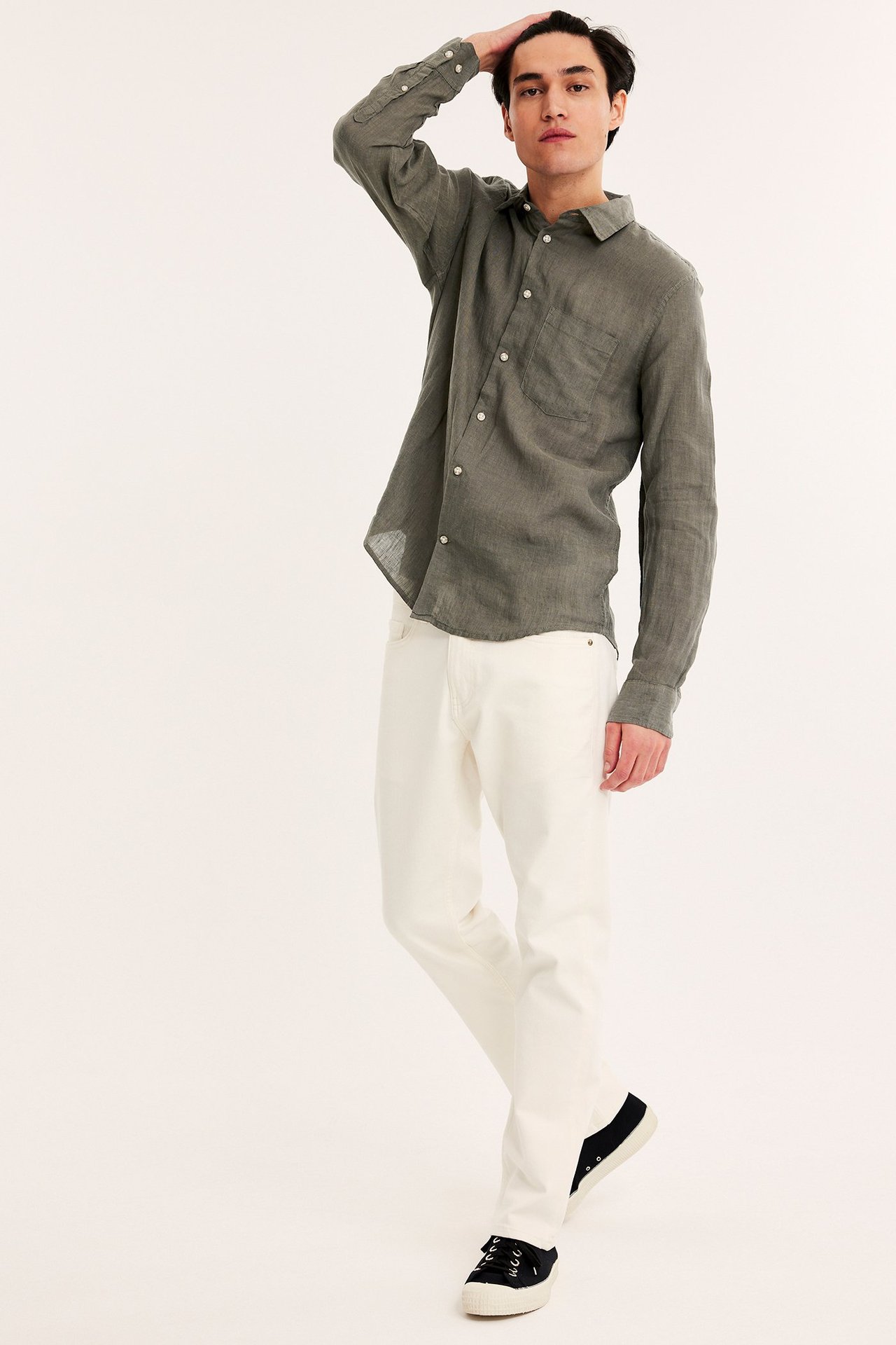 Mies edestäpäin, yllään vihreä regular fit pellavapaita, valkoiset housut ja mustat tennarit.