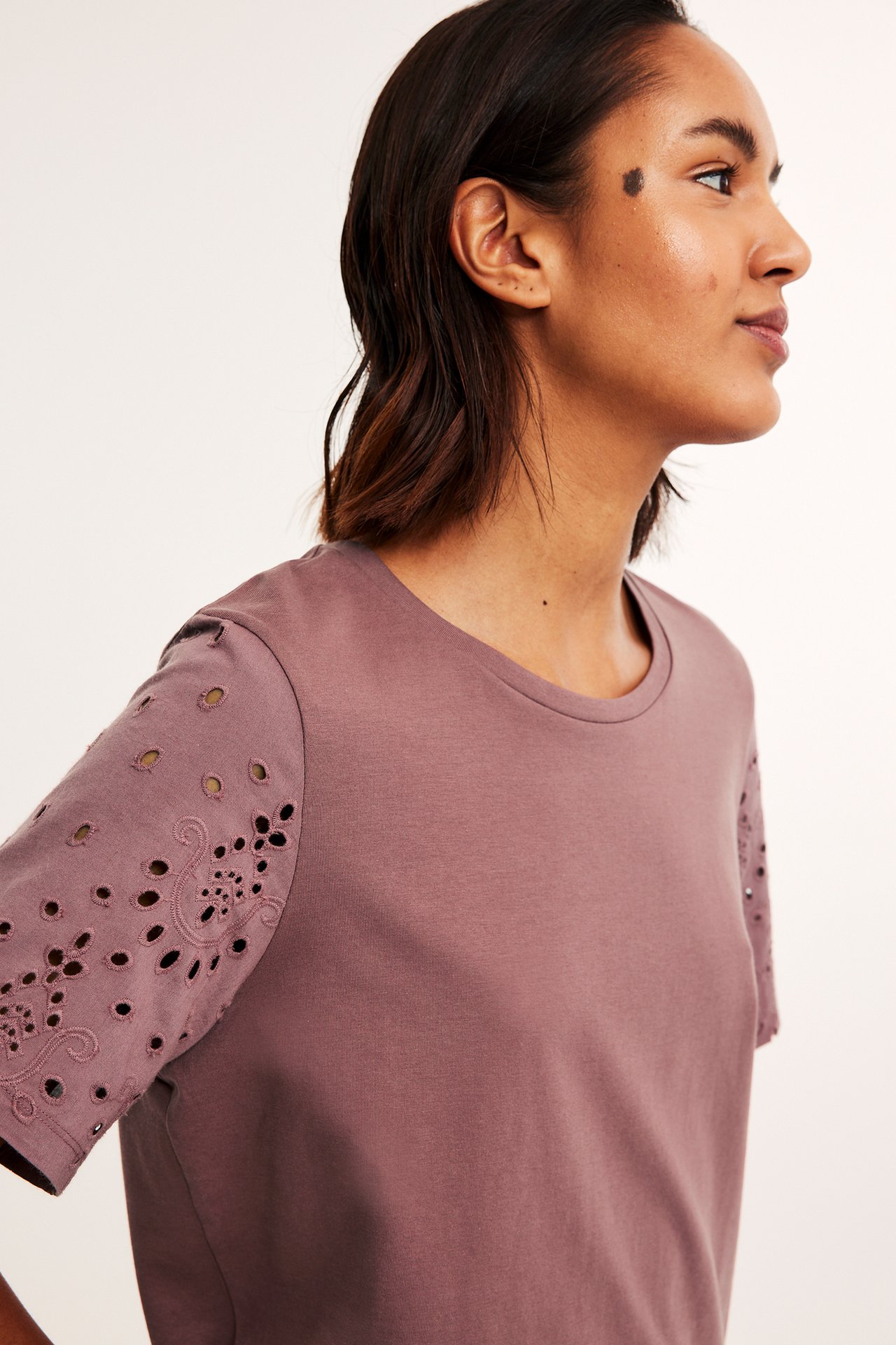 Sidovy av en kvinna i en mörkröd bomulls-T-shirt med korta ärmar i broderie anglaise.