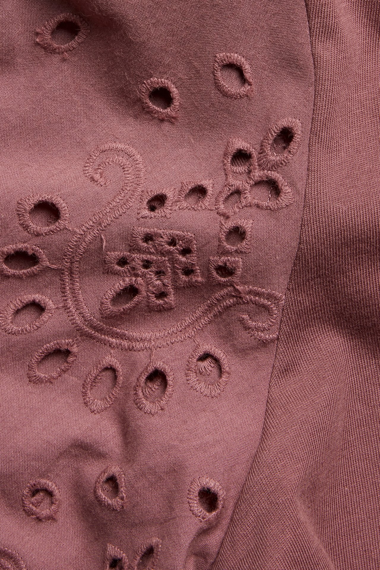 Närbild av en mörkröd T-shirt i bomull med intrikata broderie anglaise-broderier och utskurna detaljer.