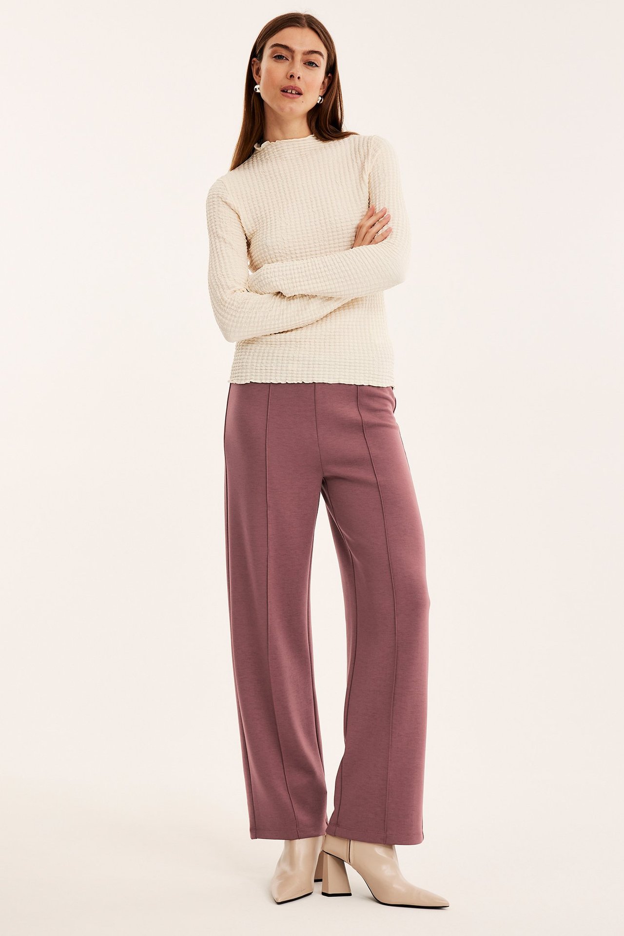 Frontvisning: kvinne i mørkerøde vide jerseytights, en kremfarget teksturert topp og lysebeige ankelstøvler.