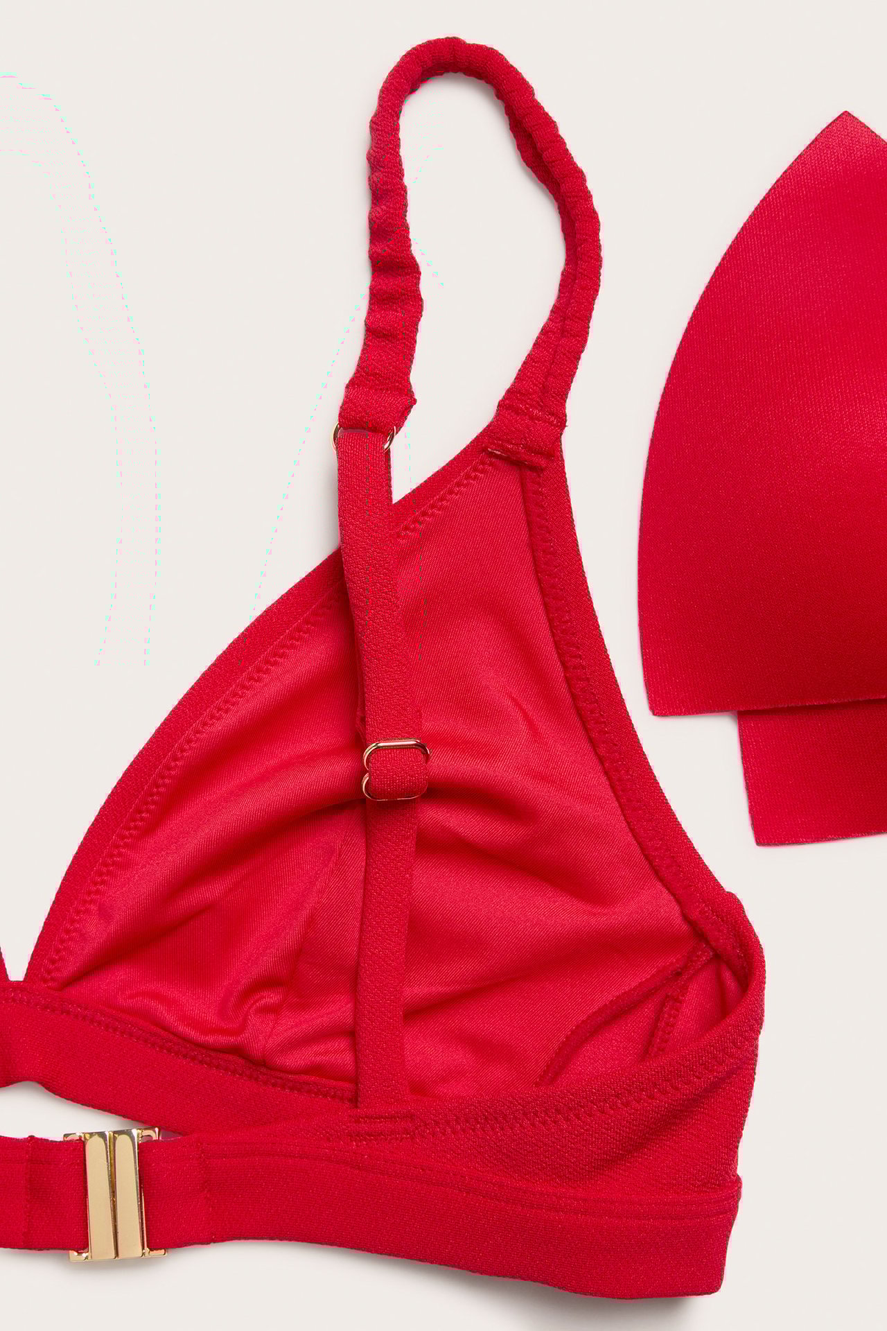 Zbliżenie czerwonego, strukturalnego biustonosza bikini z regulowanymi ramiączkami i złotym zapięciem.