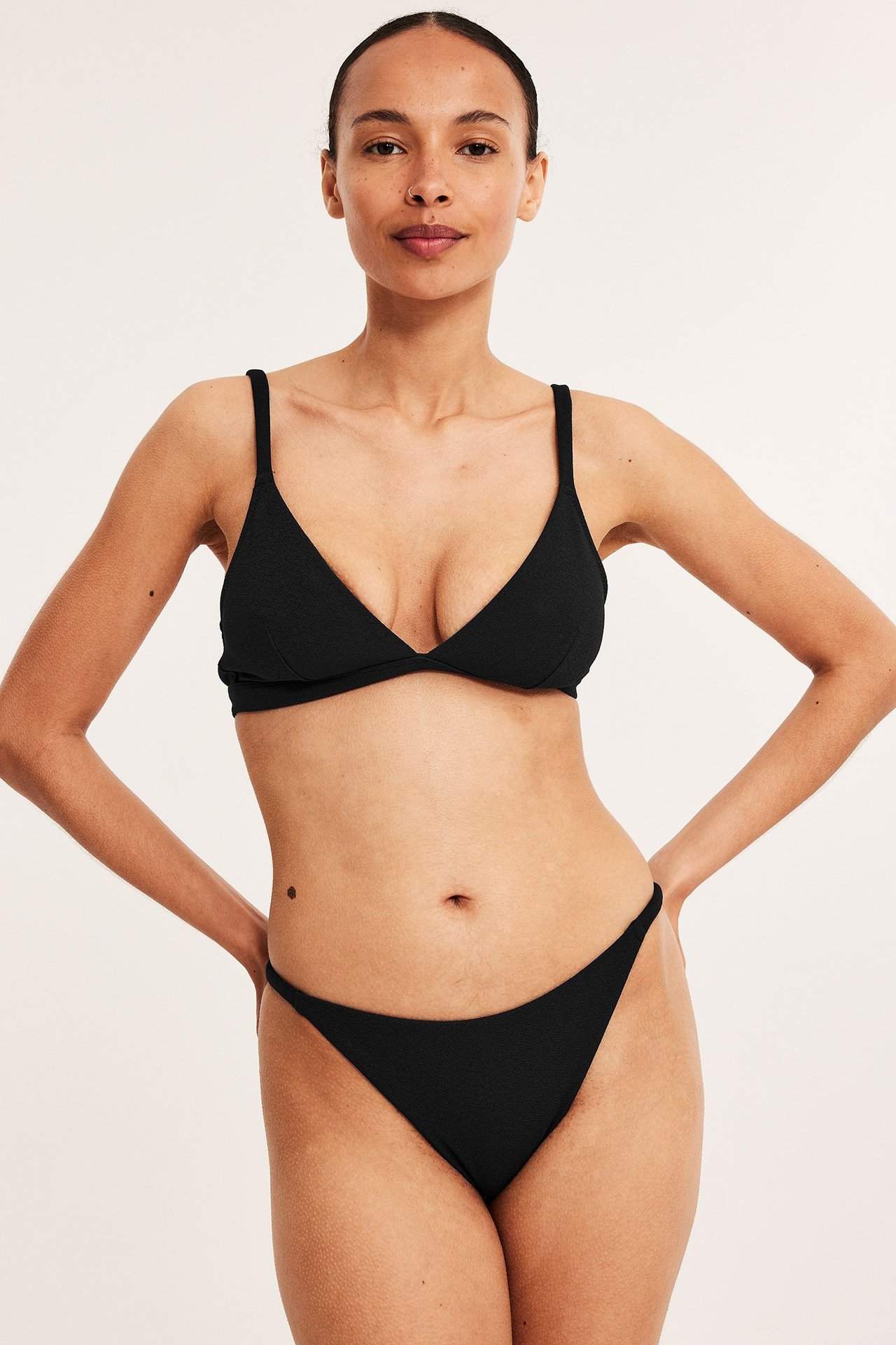 Frontbilde av en kvinne i svart strukturert bikini-BH med justerbare stropper og matchende bikinitruse.