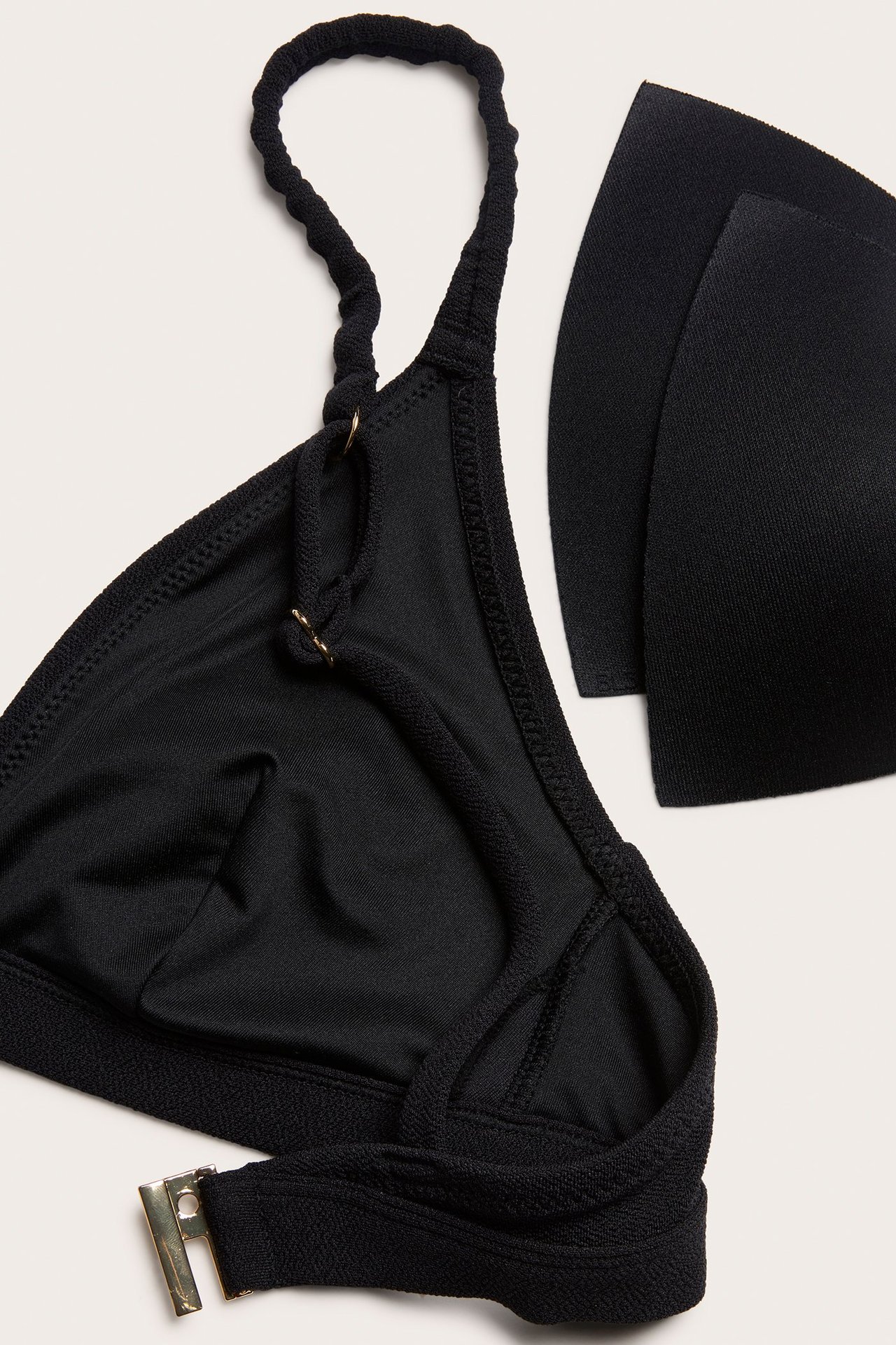 Zbliżenie: Czarny teksturowany biustonosz bikini z regulowanymi ramiączkami, złotym zapięciem i dwoma czarnymi wkładkami.