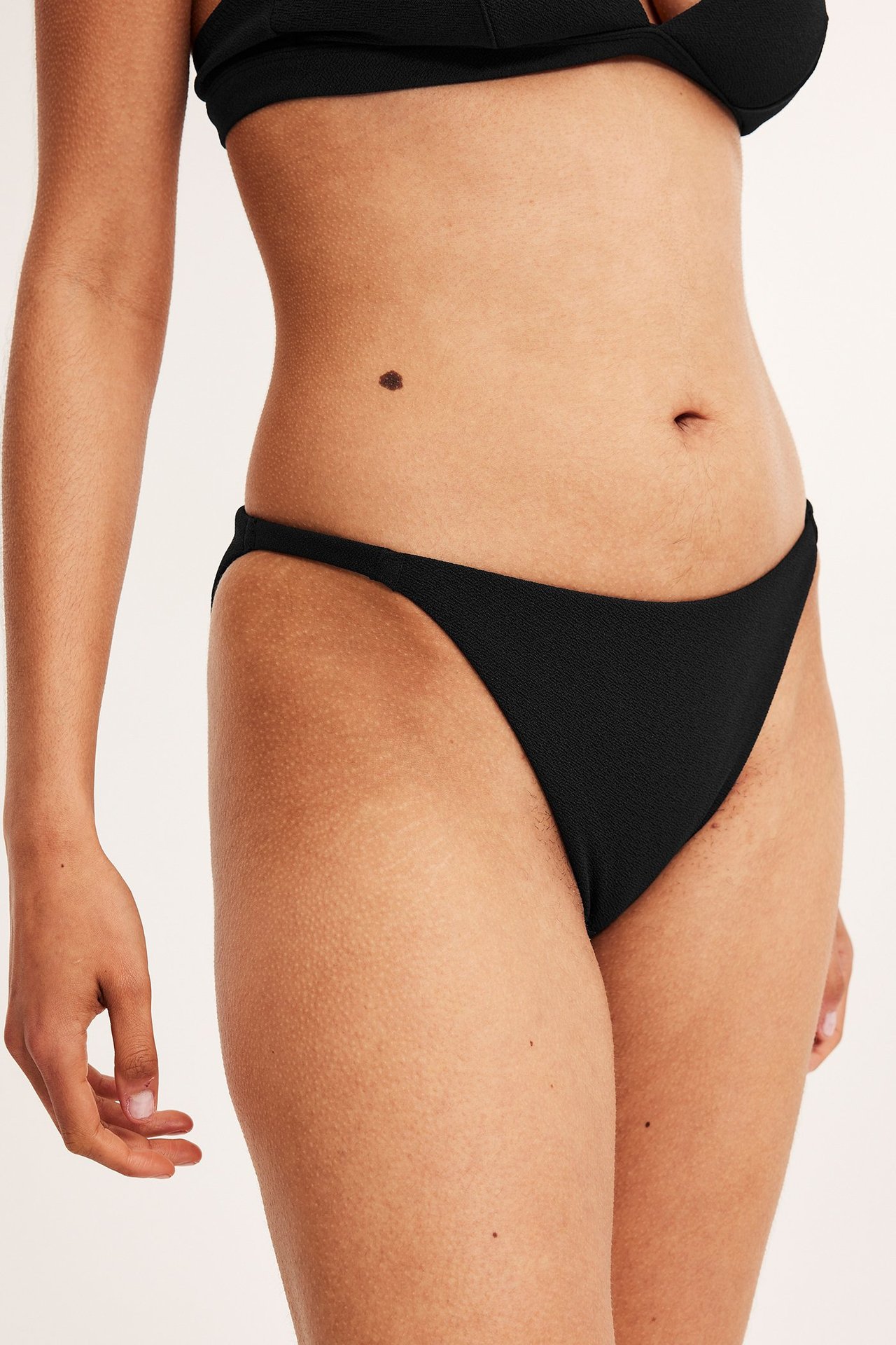 Forfra, kvinne i svart strukturert brazilian bikinitruse med smale sidebånd og matchende topp.