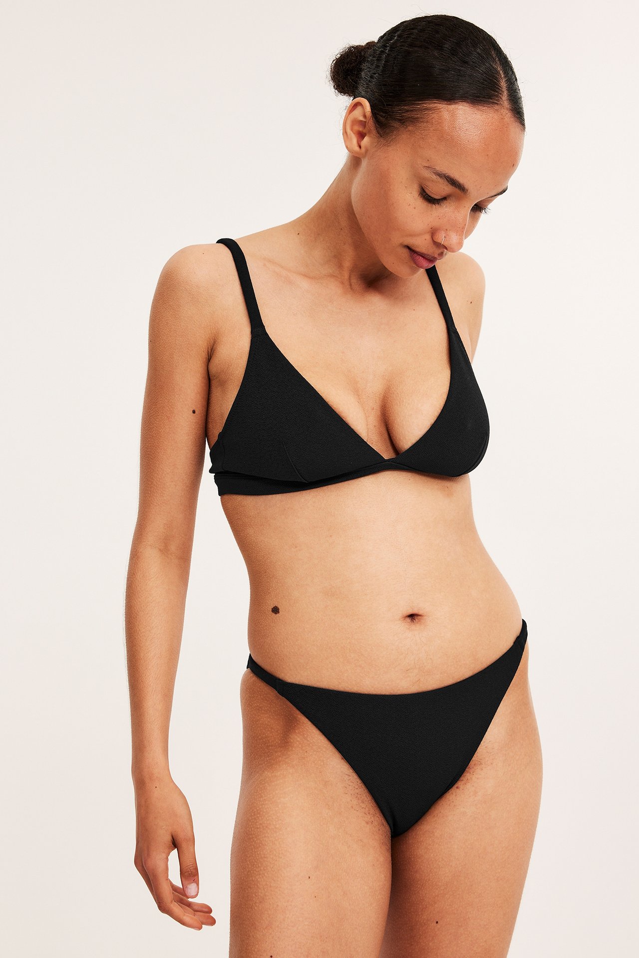 Widok z przodu: kobieta w czarnych, teksturowanych figach brazilian i pasującym biustonoszu trójkątnym.