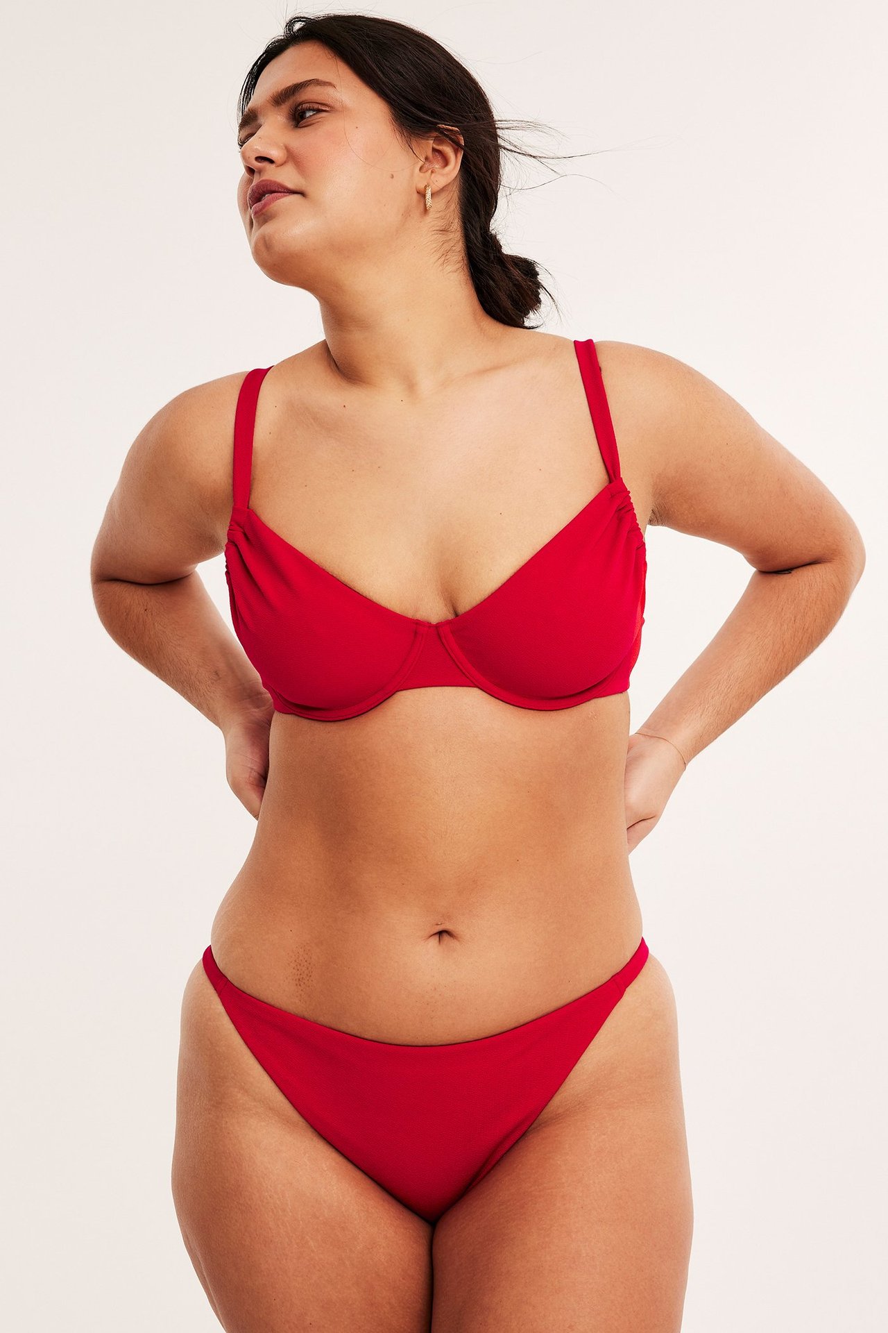 Framifrån, kvinna i röd strukturerad bygel-bikini-bh med justerbara axelband och matchande bikiniunderdel.