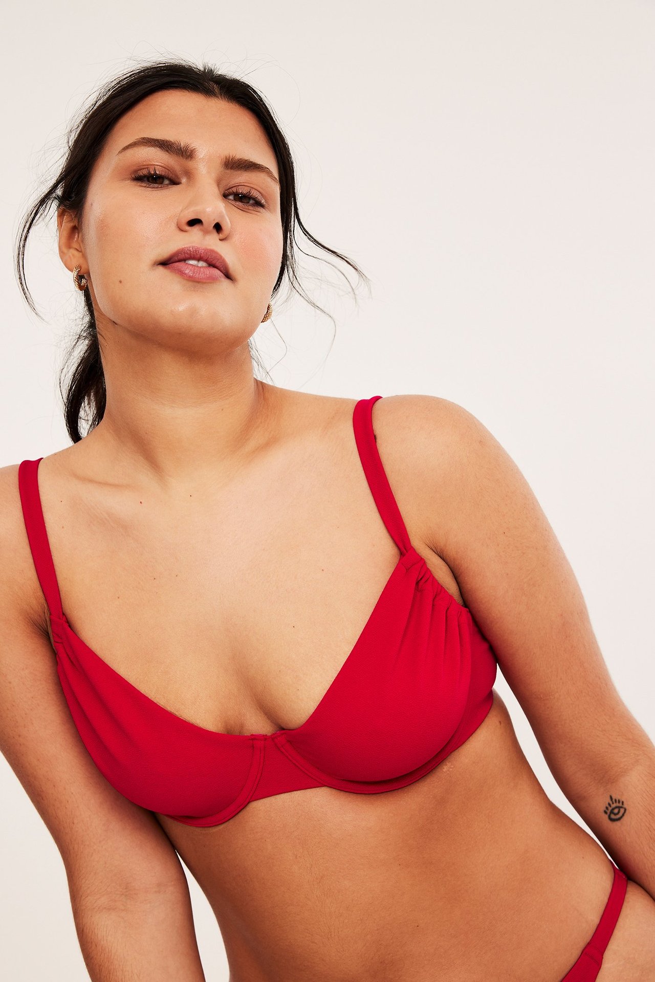 Zbliżenie z przodu kobiety w czerwonym, teksturowanym biustonoszu bikini z fiszbinami, regulowanymi ramiączkami i pasującymi majtkami.