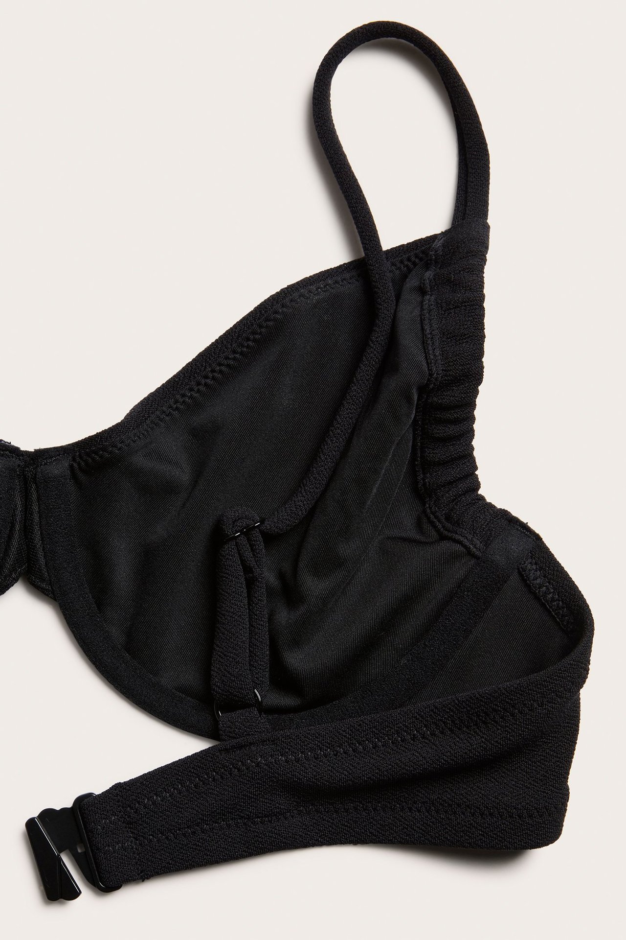 Zbliżenie czarnego, teksturowanego biustonosza bikini z fiszbinami, regulowanym ramiączkiem i plastikowym zapięciem.