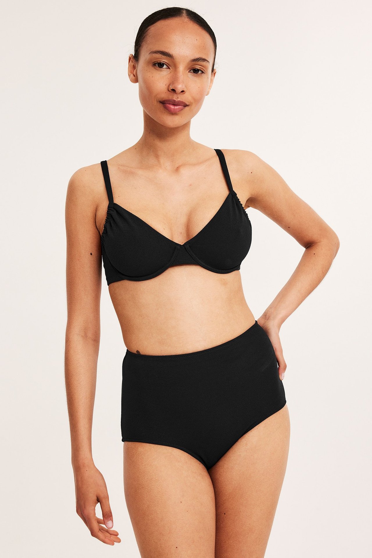 Widok z przodu kobiety w czarnym, teksturowanym biustonoszu bikini z fiszbinami i pasujących majtkach high-waist.